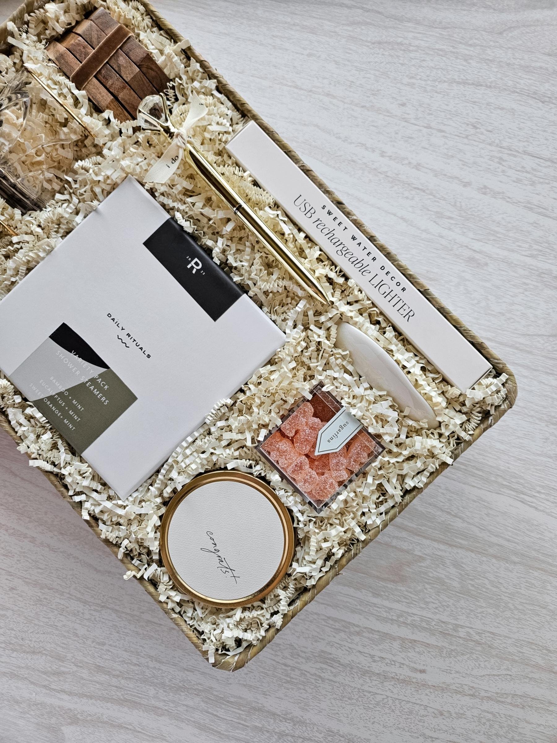 Elegant newlywed gift basket featuring rose‑tinted glasses, congrats candle, coasters, USB lighter, champagne gummies, and Mrs. ring dish.