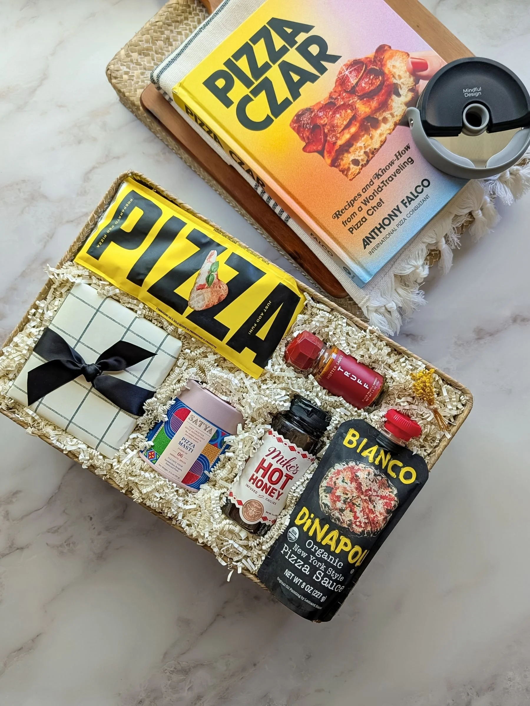 Colorful Pizza Night gift basket with Pizza Czar book, gourmet sauces, spices, dough mix, and pizza tools arranged in a seagrass basket.