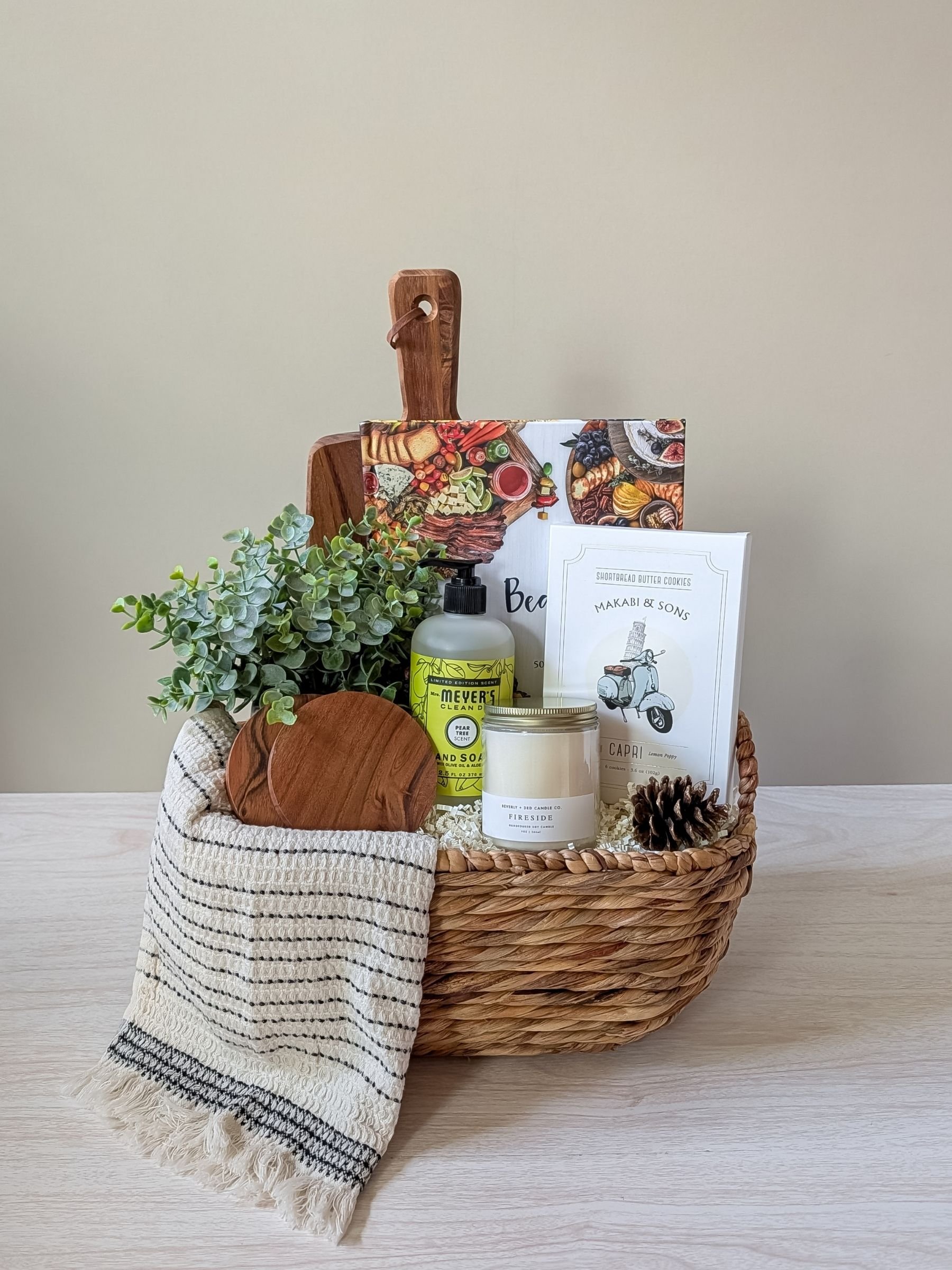 Beautiful Boards housewarming gift basket with serving board, cookbook, candle, and curated home essentials arranged in a woven gift basket.