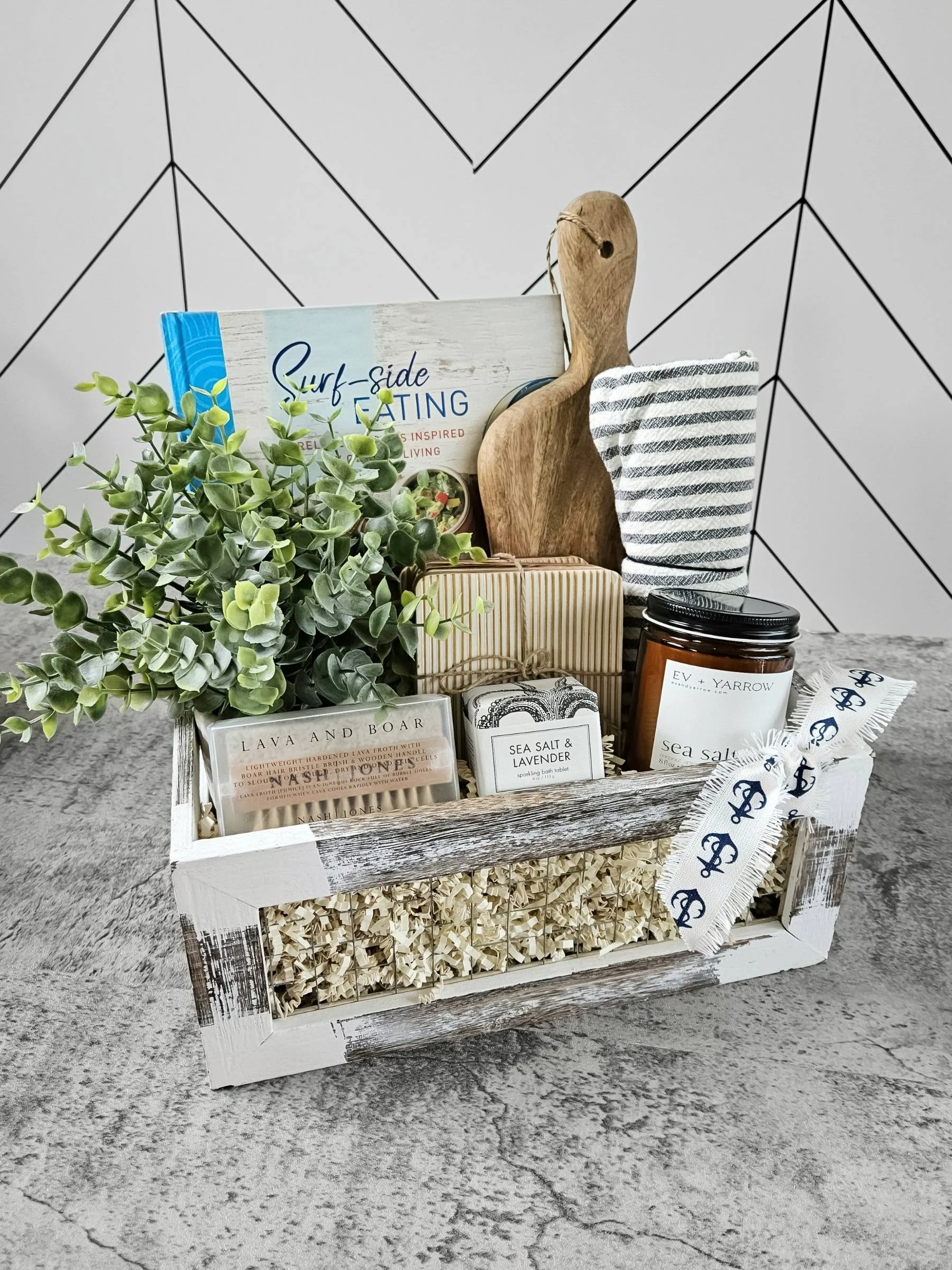 Luxury coastal gift basket with Surf‑Side Eating cookbook, driftwood board, boar & lava pumice brush, sea salt bath tablet, candle, and home essentials.