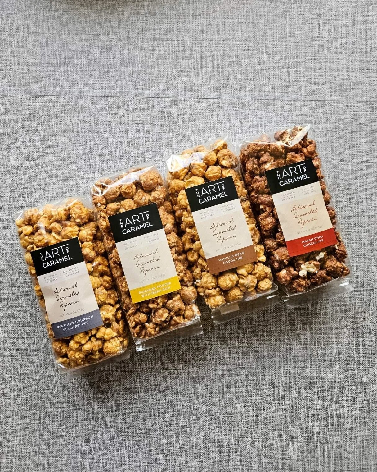 Art of Caramel gourmet popcorn bags featuring Kentucky Black Pepper Bourbon, Bananas Foster Rum, Vanilla Cocoa Nib, and Mayan Chili Chocolate flavors.