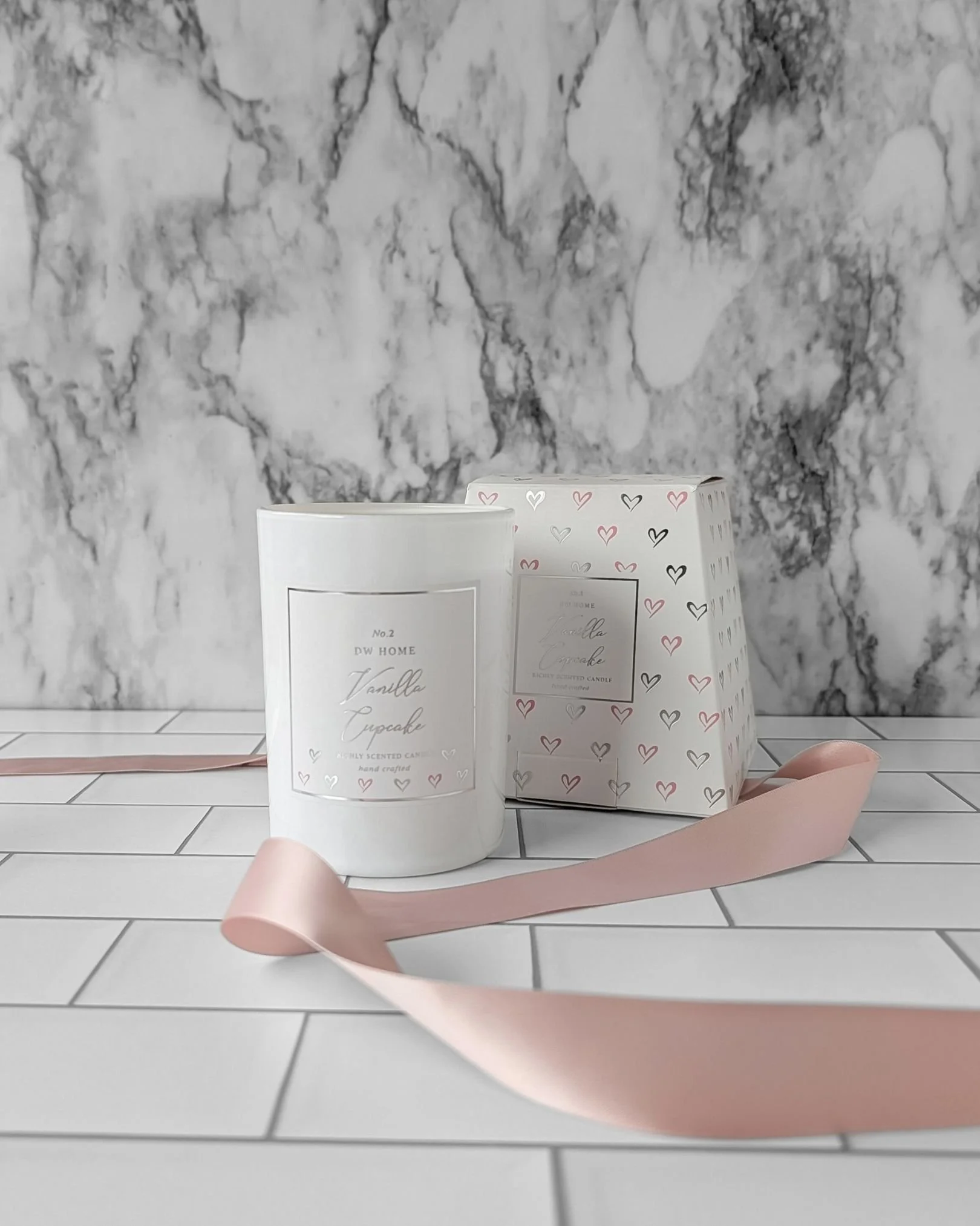 Vanilla cupcake candle displayed outside its box with blush satin ribbon draped beside it for a soft, modern birthday gift detail.