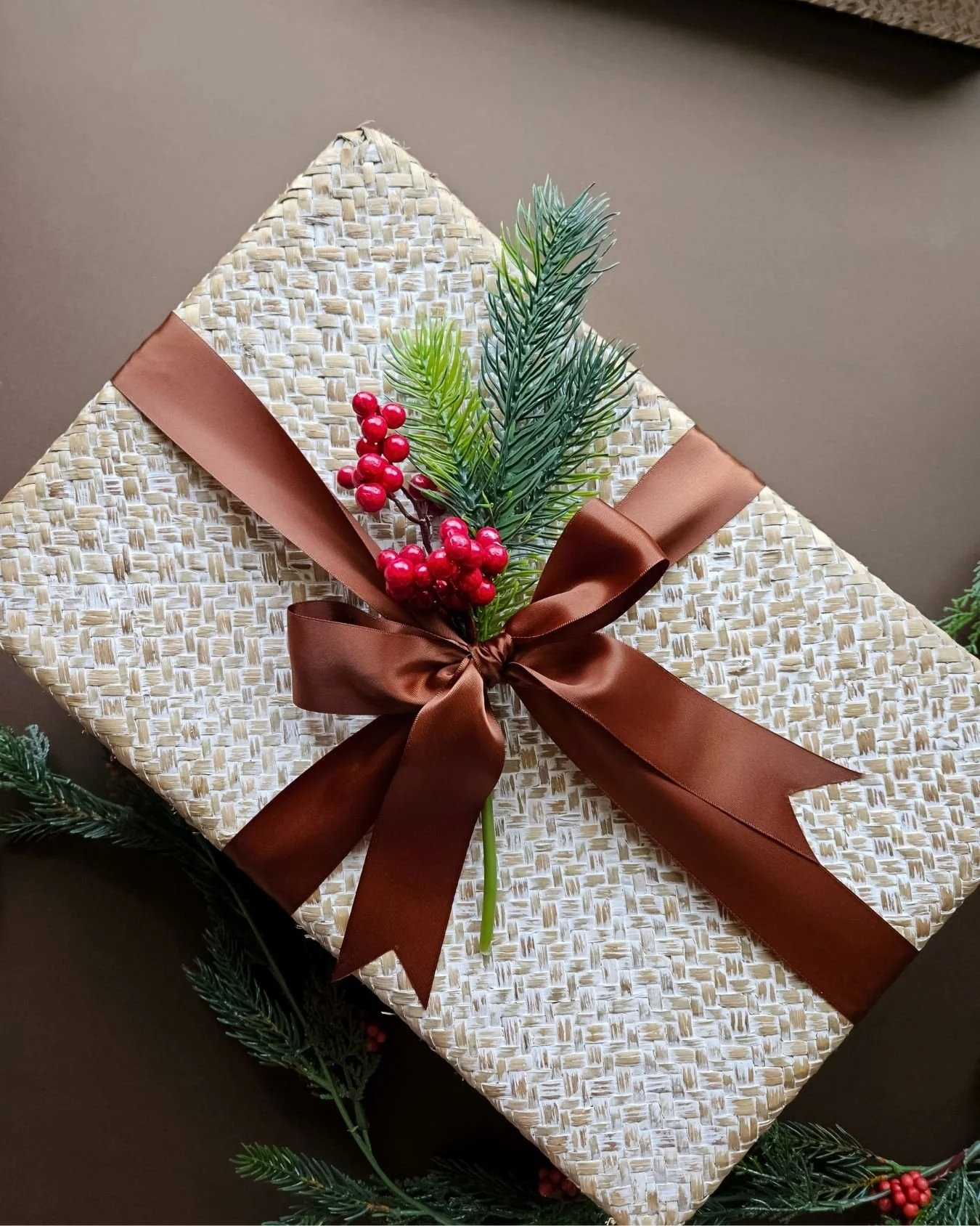 Luxury seagrass gift basket wrapped with a double satin copper ribbon and festive sprig, curated for holiday gifting and client appreciation.