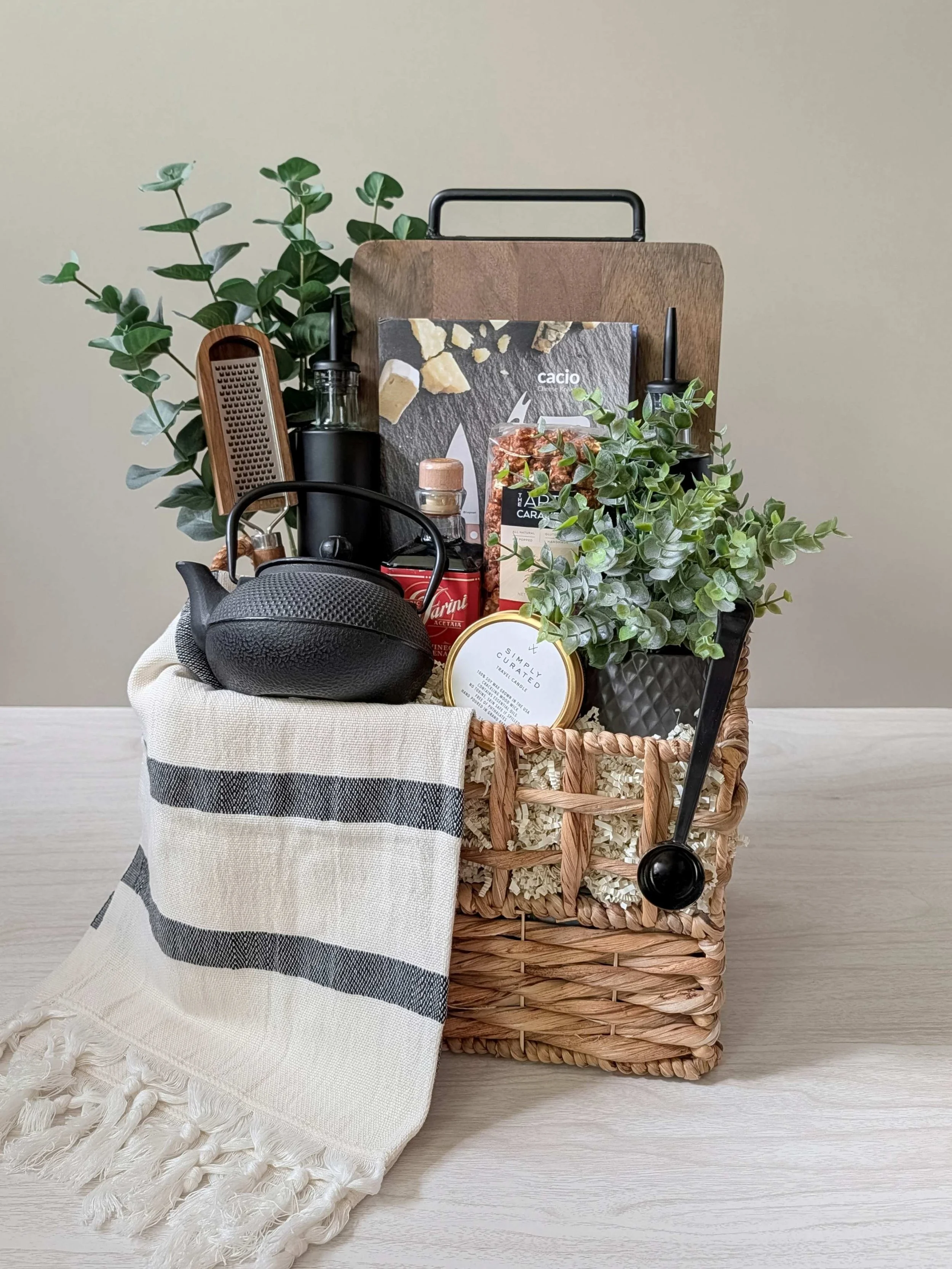 Luxury housewarming gift basket with glass oil & vinegar dispensers, cheese knives, wood serving board, Turkish tea towel, tea, and cast-iron teapot with infuser.