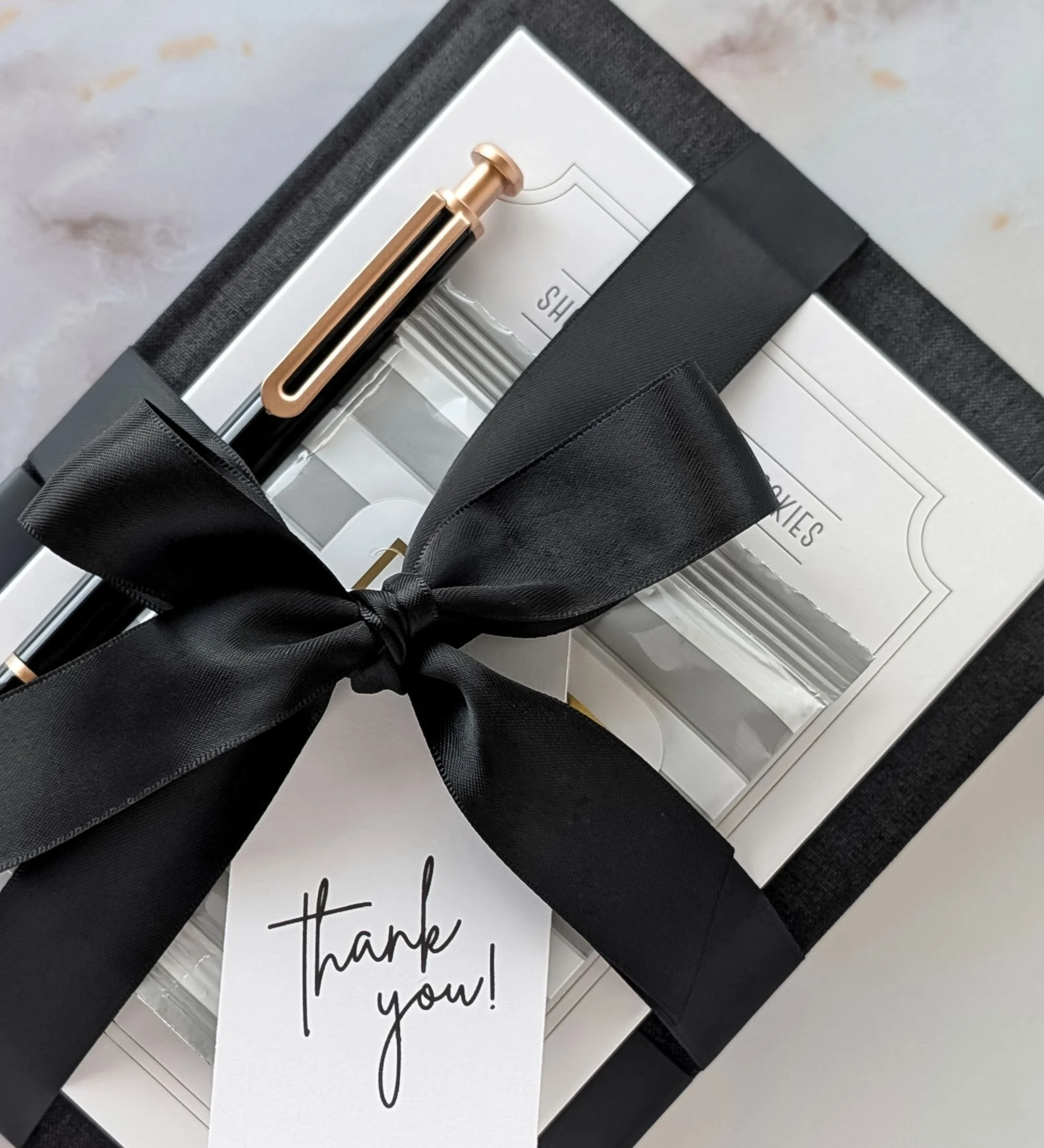 Professional client thank‑you gift featuring black linen notebook, gold pen, Makabi cookies, and modern office essentials.