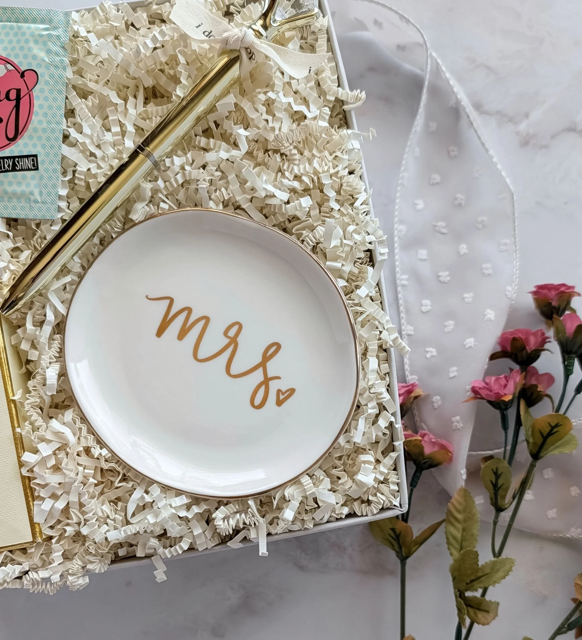 Close‑up of ‘Mrs.’ ceramic ring dish with gold lettering, gold diamond pen, and luxury California gummy bears in a bridal gift box.