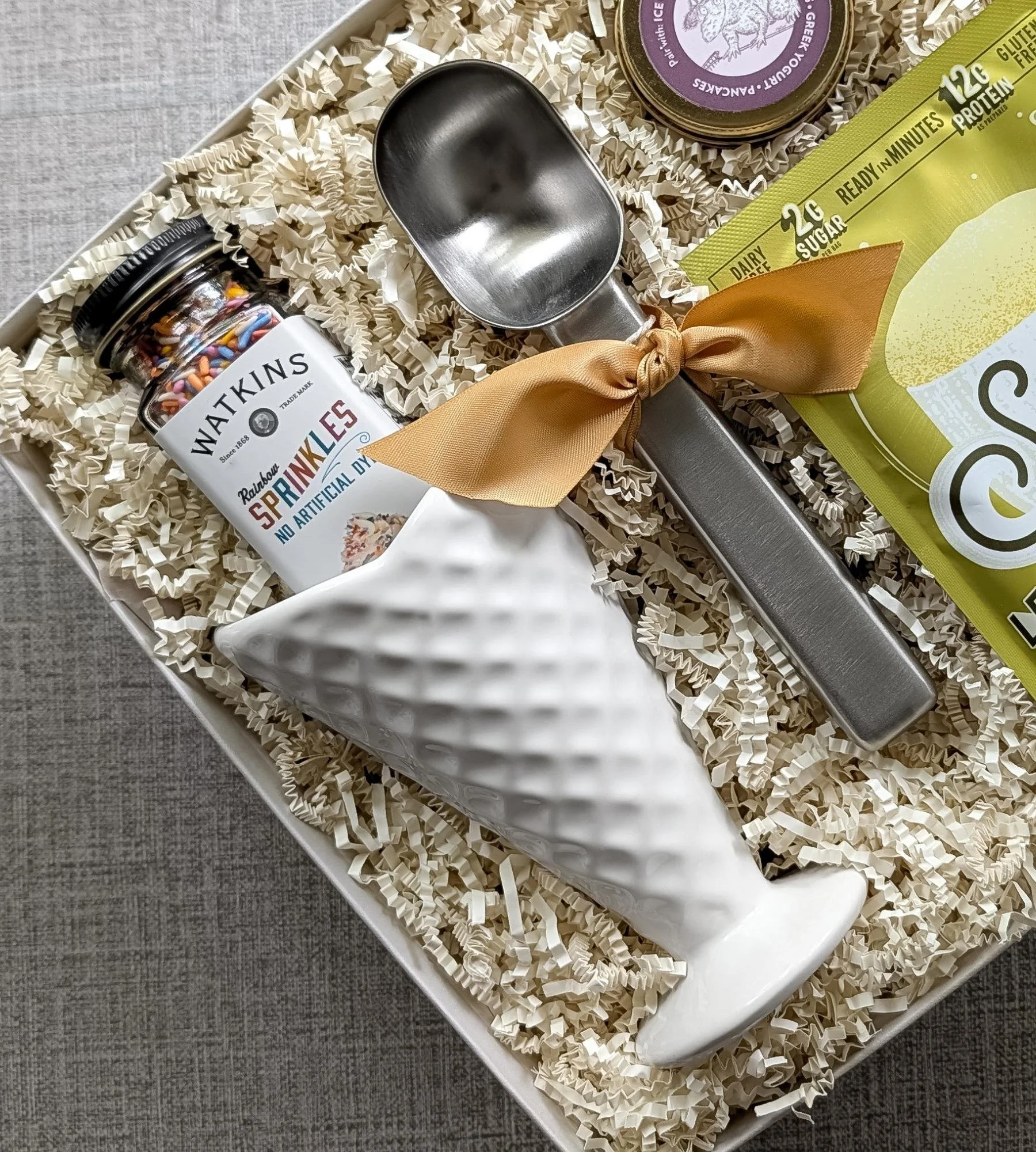 The Scoop gift set featuring a vintage white ceramic waffle bowl, rainbow sprinkles, lemon mug cake, and caramel drizzle.