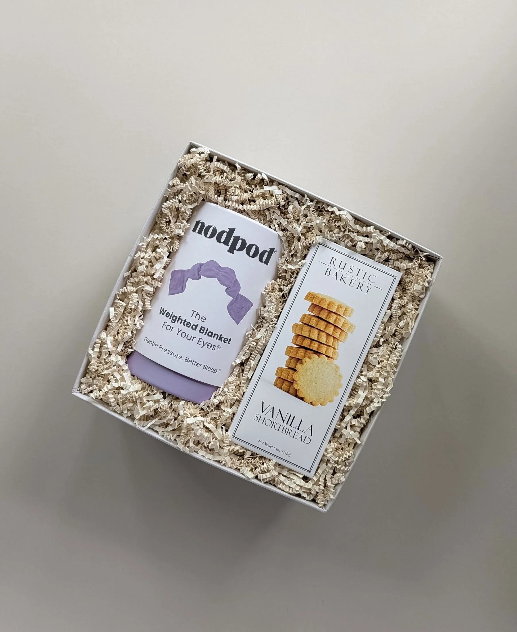 The linen retreat featuring gourmet vanilla shortbread cookies and a lavender weighted eye mask by Nodpod, nestled in a linen gift box and ivory crinkle paper.