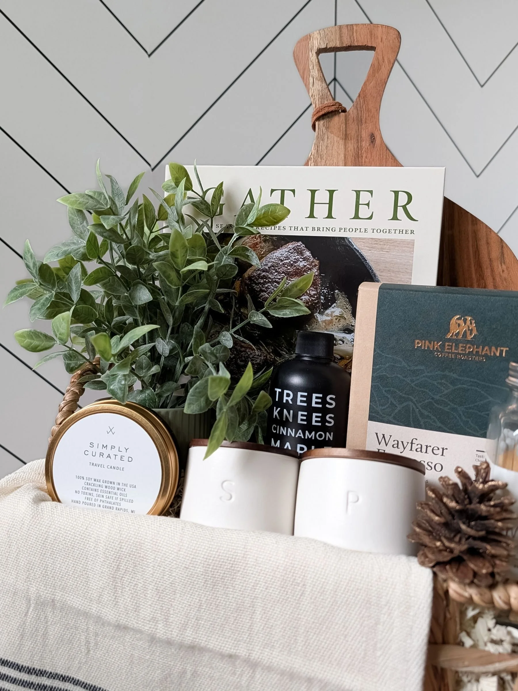 Rustic gourmet gift basket with a luxe candle, small batch maple syrup, gather cookbook, salt and pepper cellars, espresso coffee, and home décor.