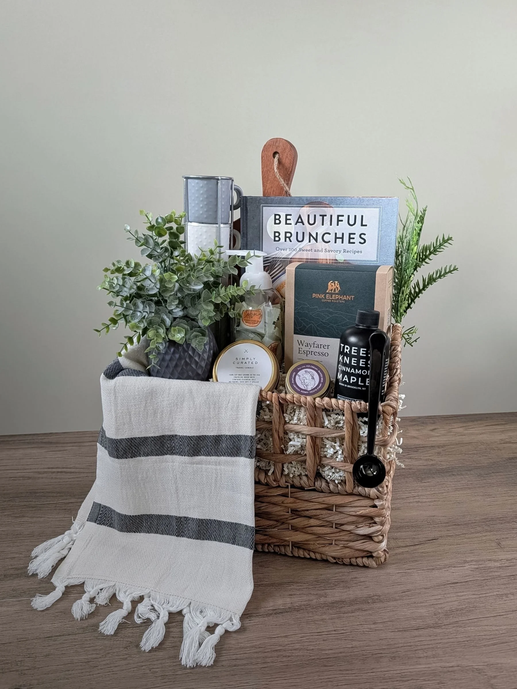 Beautiful Boards housewarming gift basket with a wood serving board, hosting cookbook, candle, striped charcoal and white Turkish hand towel, espresso mug tower, espresso coffee, and curated cozy home essentials.