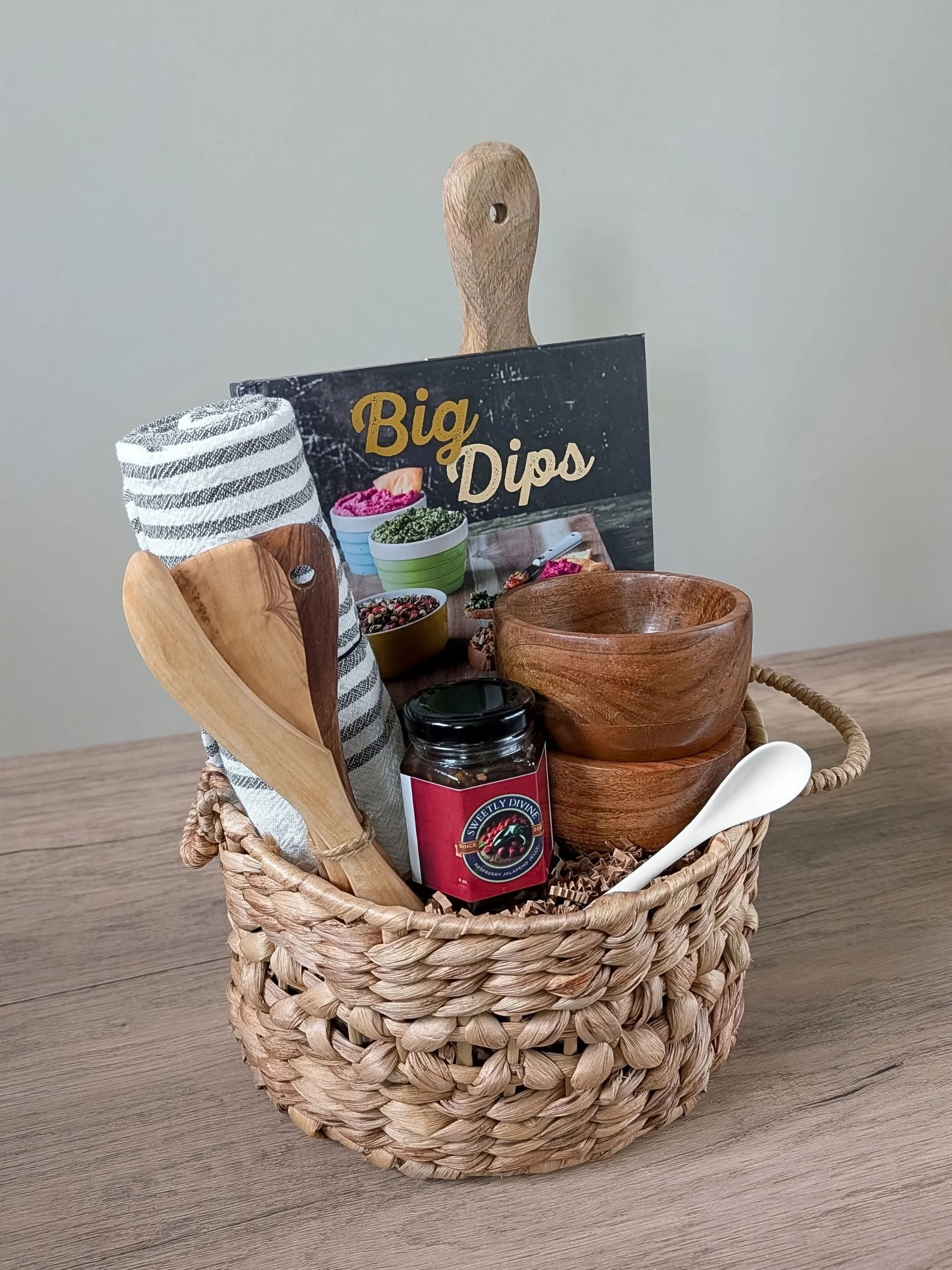 Small bites inspired apéro gift basket featuring wooden bowls, tea towel, wooden serving tools, and a Dips cookbook.