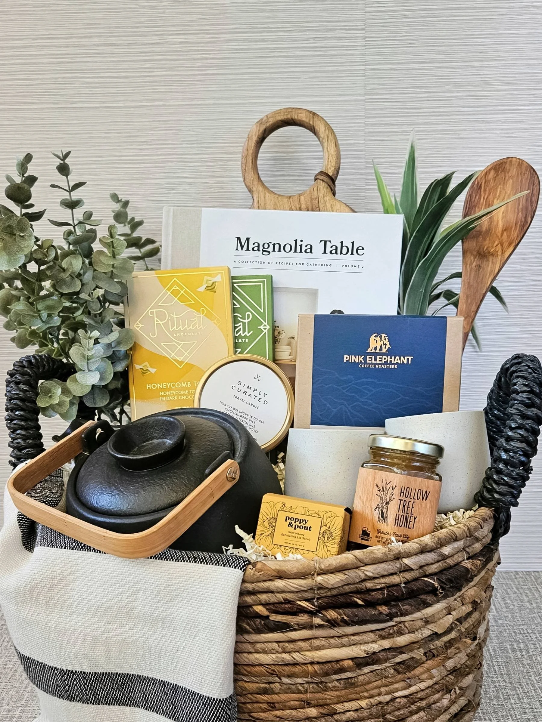 Curated sustainable gift box with a cookbook, stoneware mugs, gourmet treats, wildflower honey, a travel candle, and handcrafted home accents.