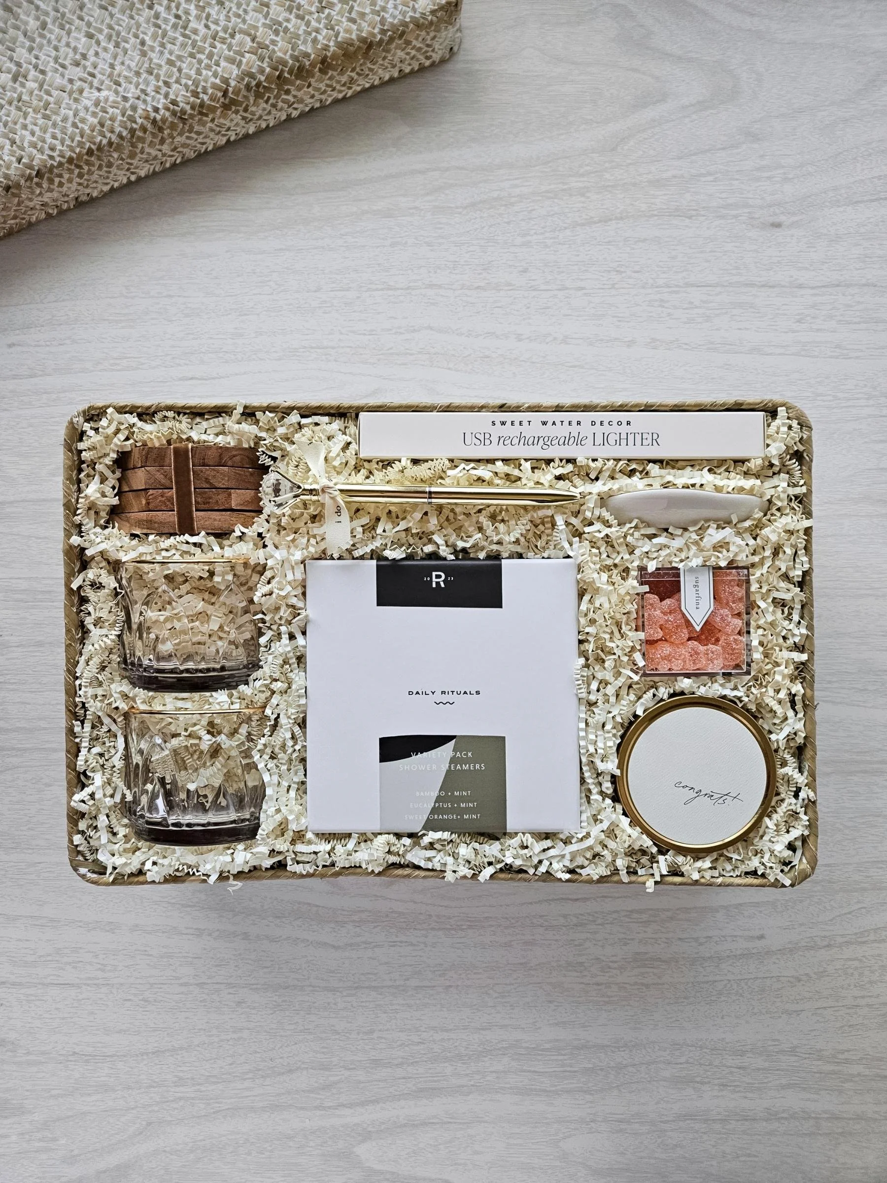 Luxury wedding gift basket with rose‑tinted glasses, congrats candle, shower steamers, ring dish, and gold ring pen for newlyweds.