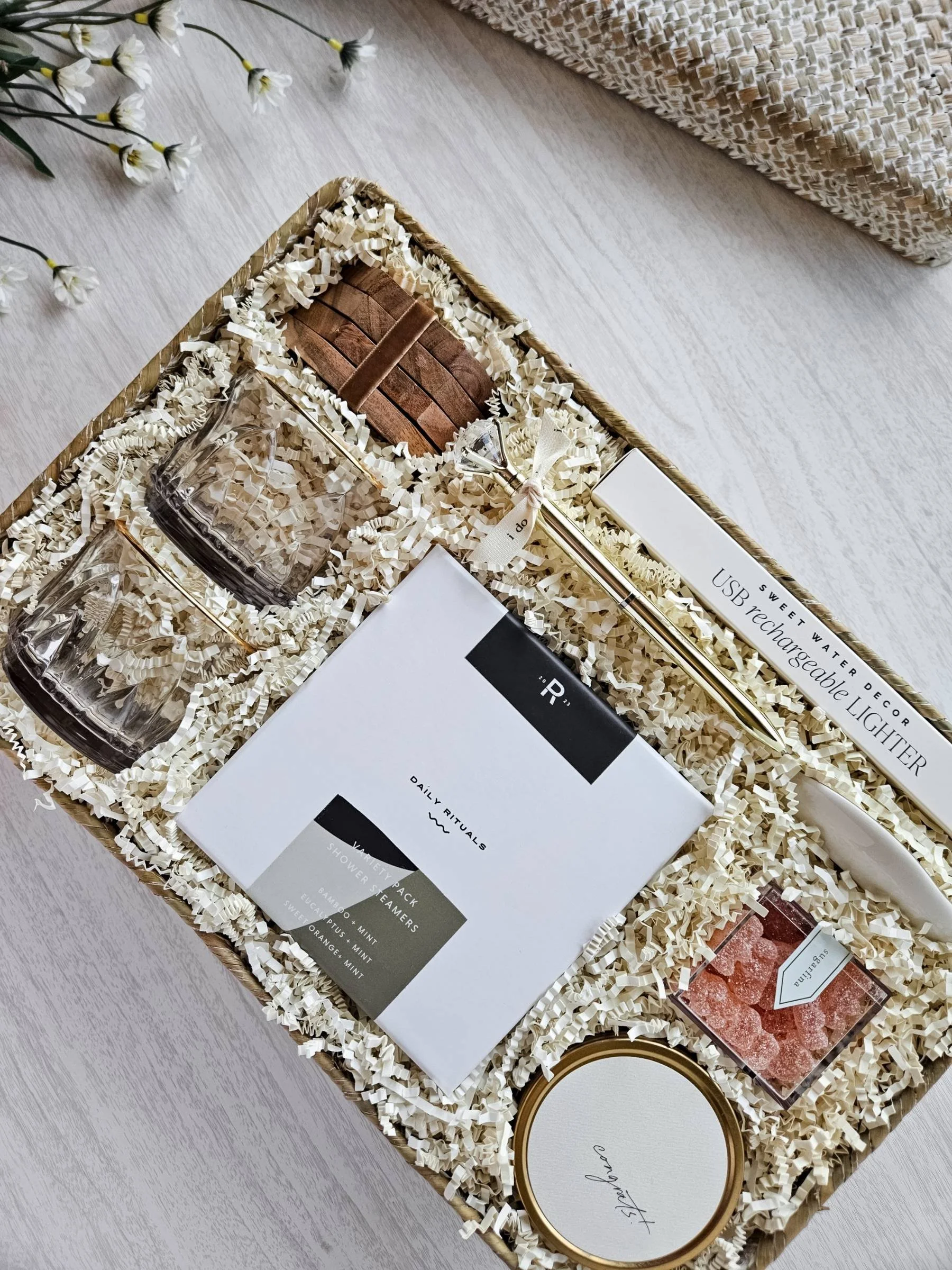 Curated wedding gift basket with rose‑tinted glasses, congrats candle, ring dish, coasters, steamers, and gold accents for celebrating newlyweds.