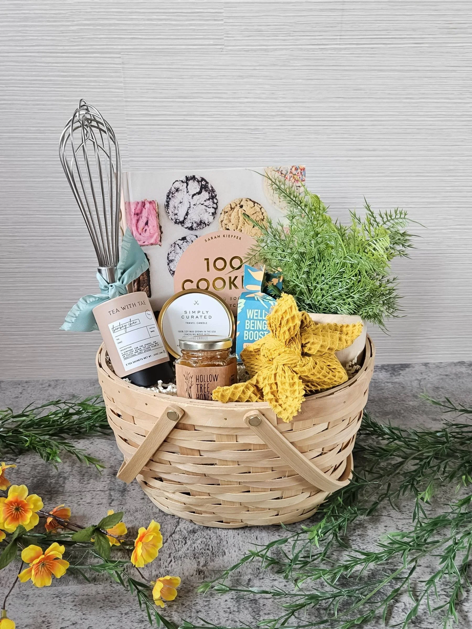 Spring gift basket perfect for Mother's Day with wildflower honey, chai tea, seed bomb, 100 cookies cookbook, candle, hand soap, and whisk.