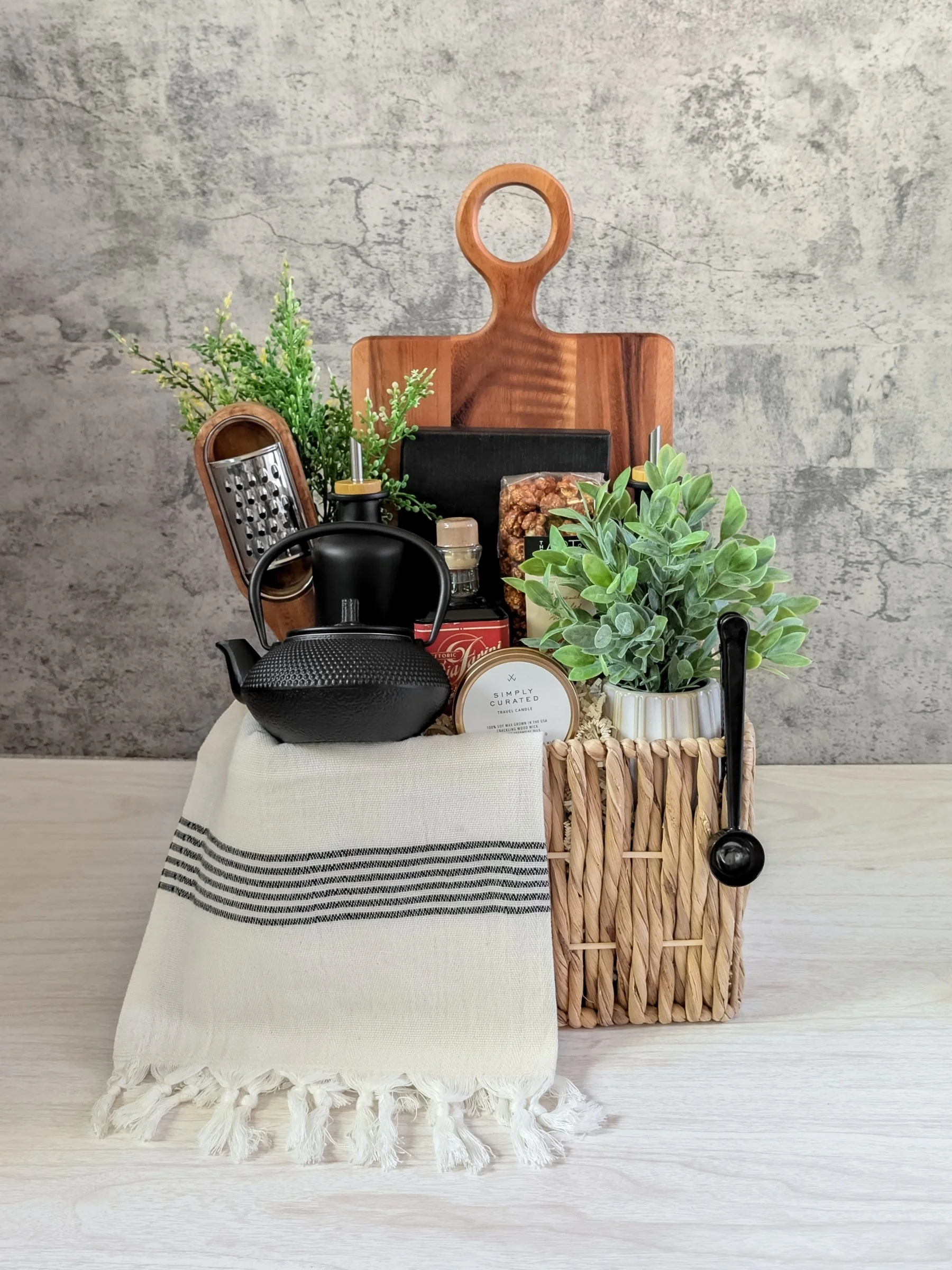 Luxury housewarming gift basket with glass oil & vinegar dispensers, cheese knives, wood serving board, Turkish tea towel, tea, and cast-iron teapot with infuser.