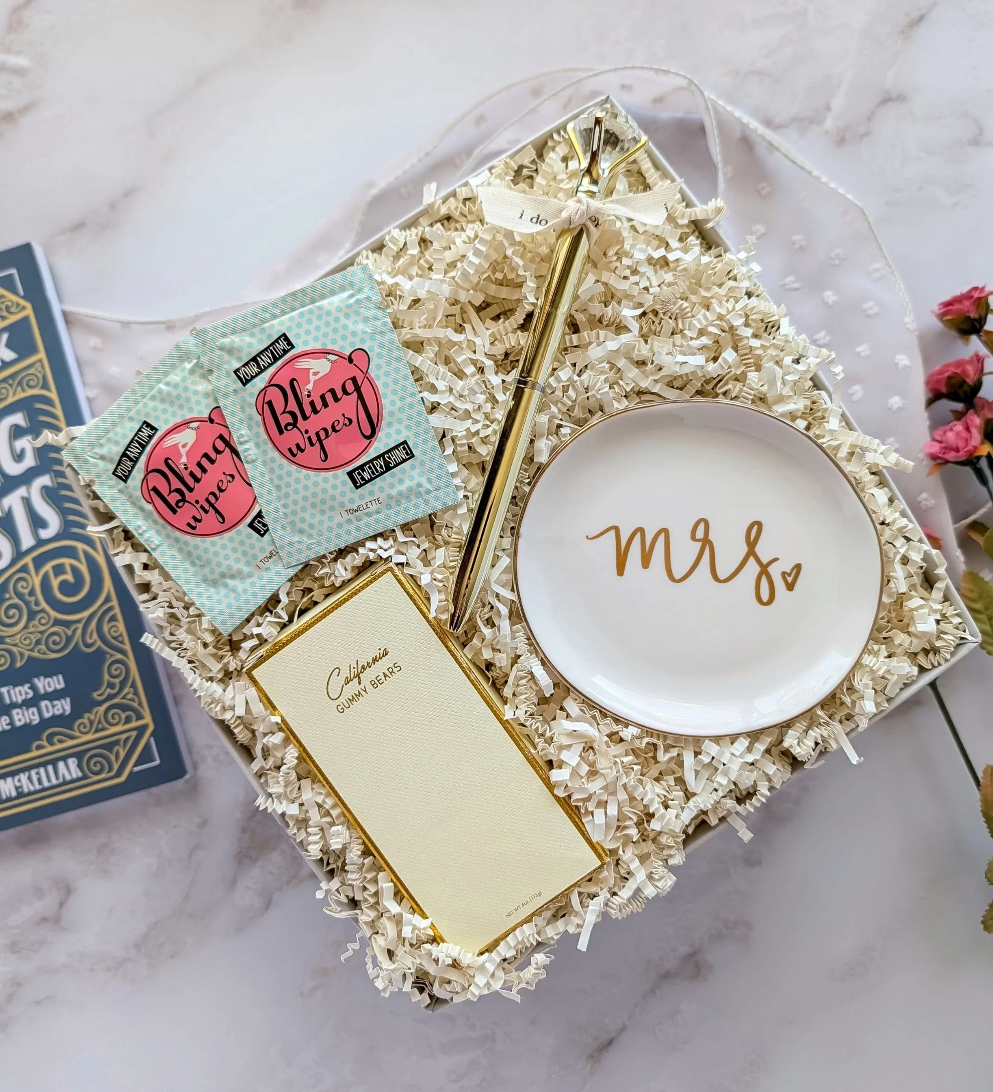 The Blush engagement gift box featuring Bling Ring wipes, California gummies, ‘Mrs.’ ring dish, gold diamond pen with ‘I do’ ribbon, and wedding checklist book.