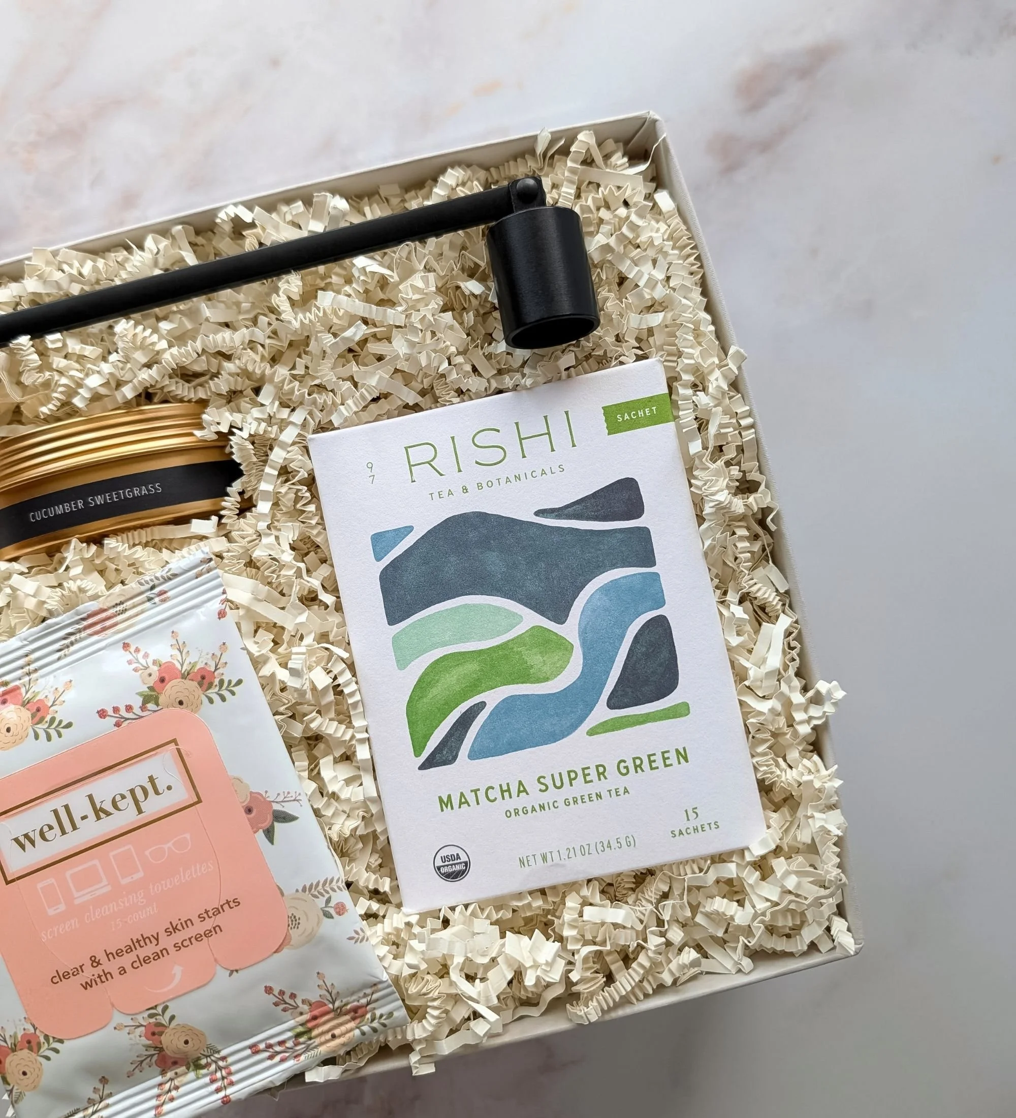 Uplifting gift box for her including matcha tea, floral wipes, a modern candle snuffer, and a cucumber sweet grass candle.