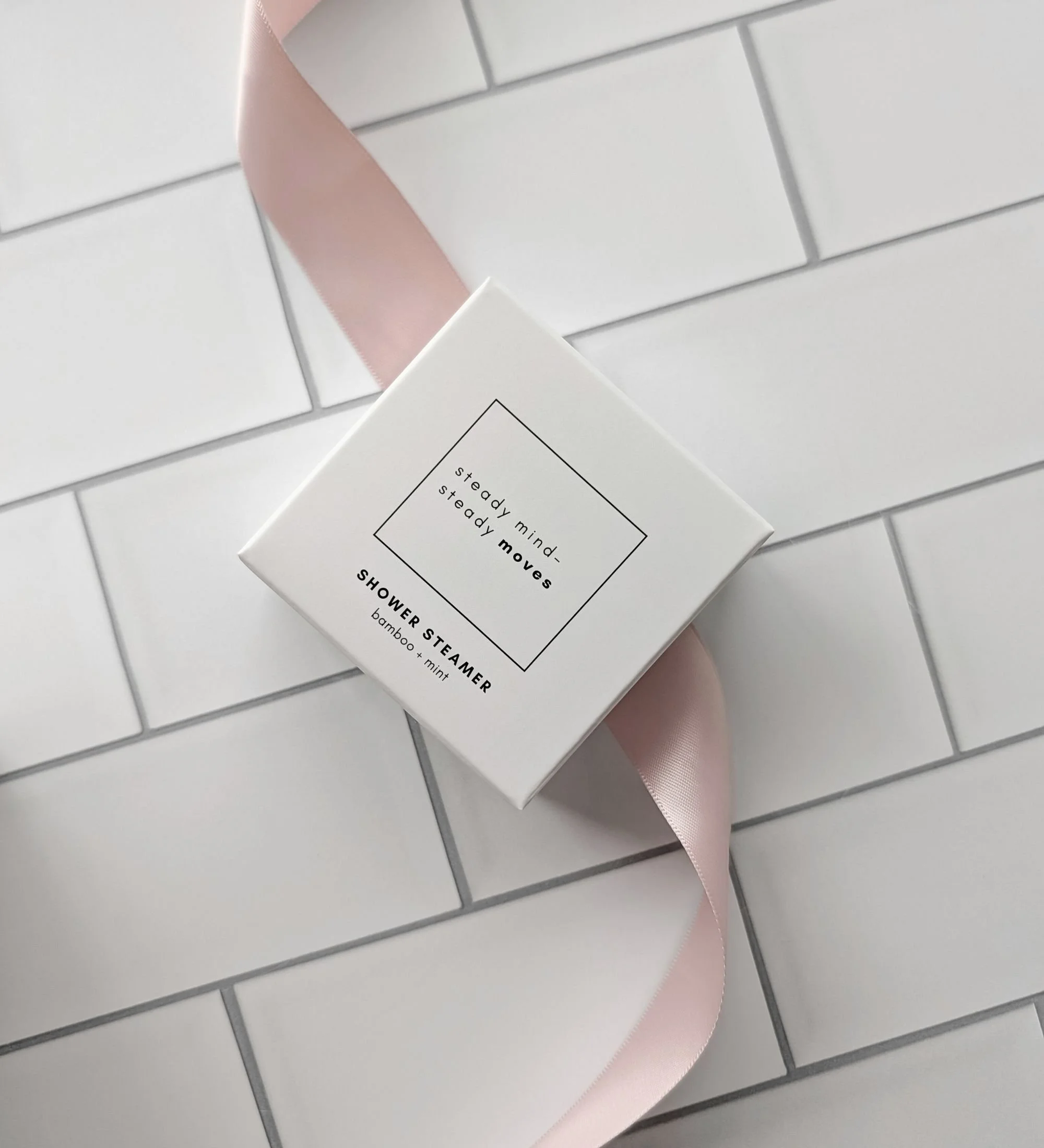 Blush satin ribbon styled with a bamboo mint shower steamer for a soft, modern birthday gift flatlay in warm neutral tones