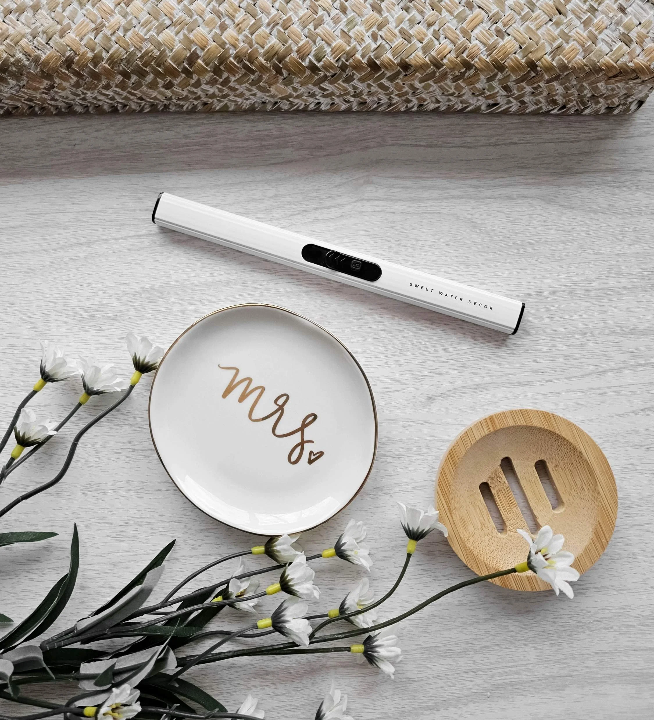 Bridal gift flatlay with white USB lighter, “Mrs.” ring dish, and bamboo shower‑steamer tray from The Vow wedding gift box.