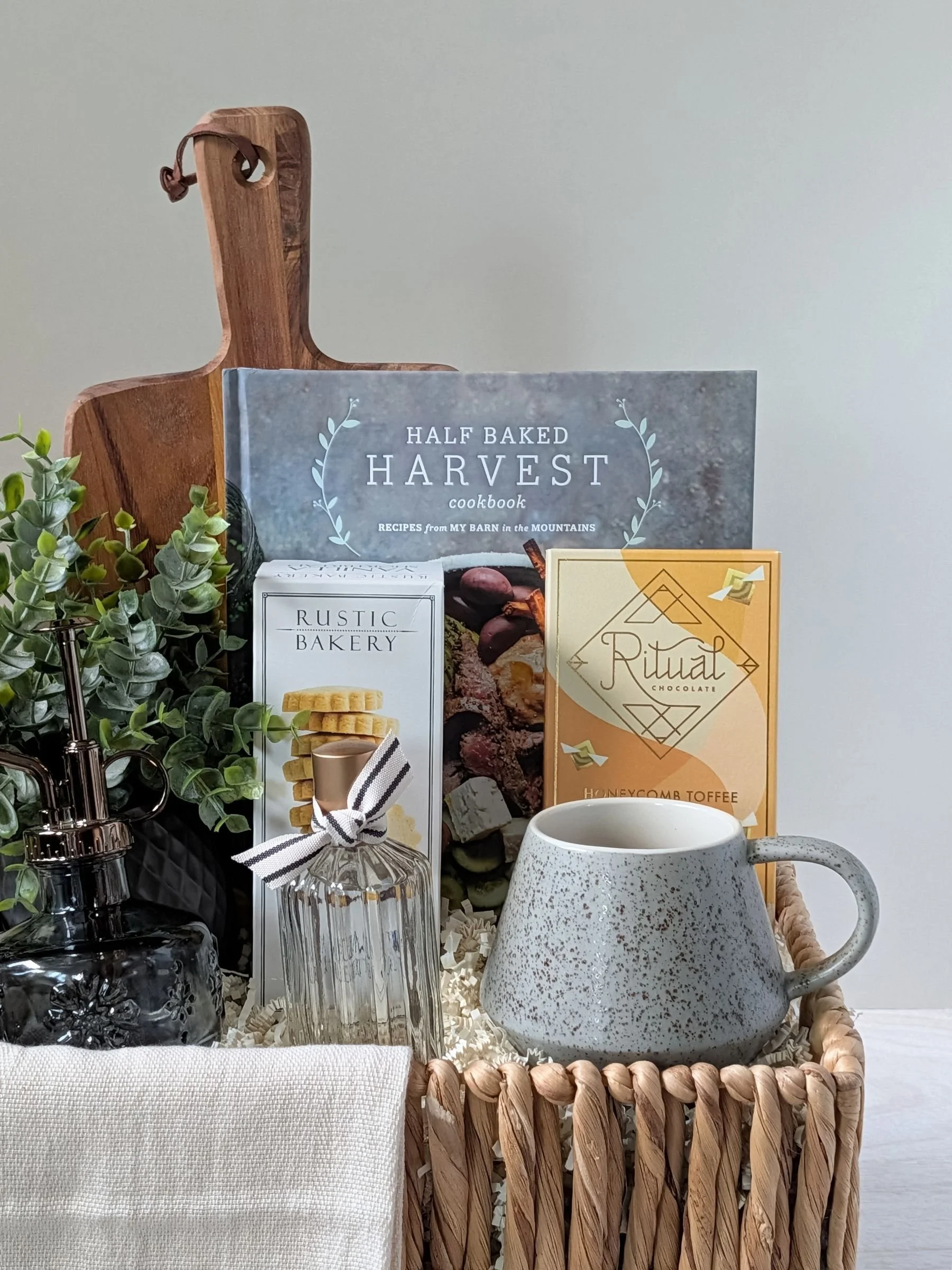 Luxury home gift basket featuring cookbook, gourmet chocolate, cookies, linen spray, Turkish towel, artisan mug, and décor accents.