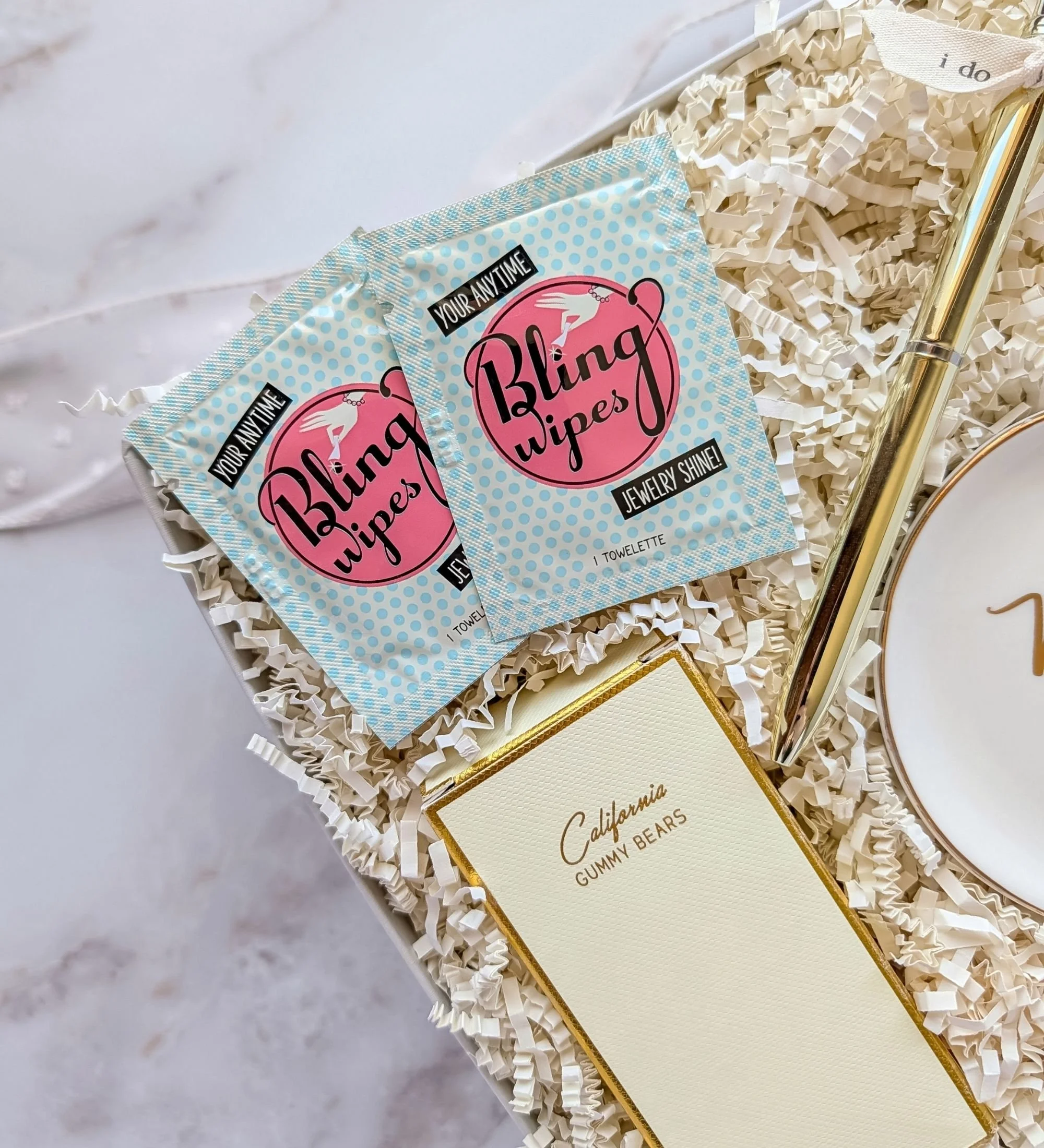 Detail shot of two Bling Ring wipes and California gummy bears inside a luxe gold linen bridal gift box.