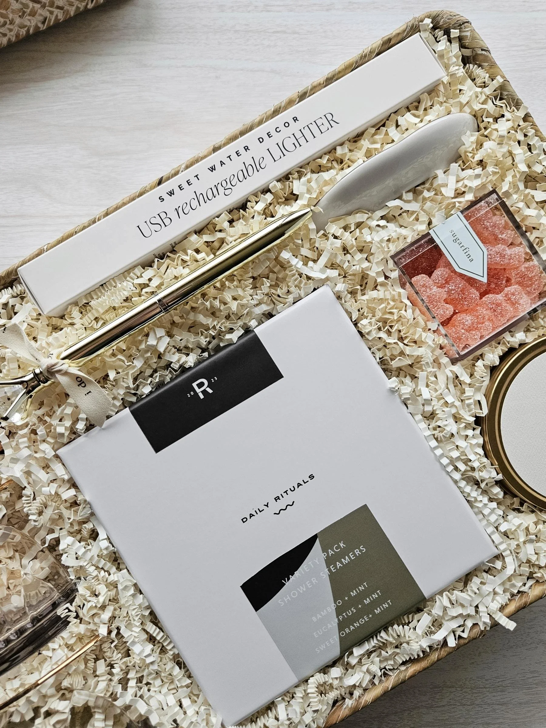 Modern wedding gift basket including luxe glasses, shower steamers, congrats candle, gold ring pen, USB lighter, and champagne gummies.