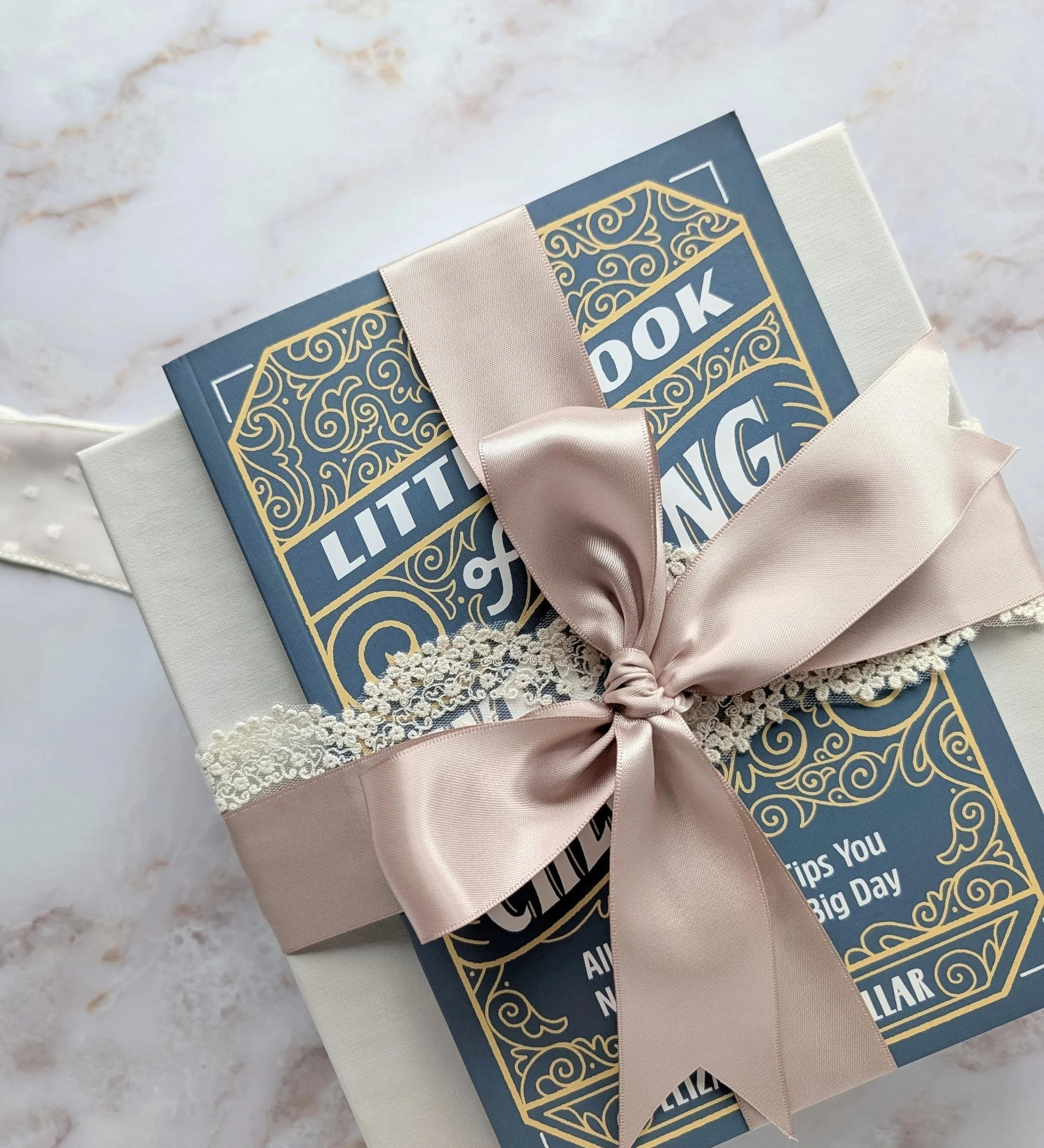 Close‑up of wedding checklist book tied on a linen gift box with lace ribbon and mauve satin bow for a luxury bridal gift.