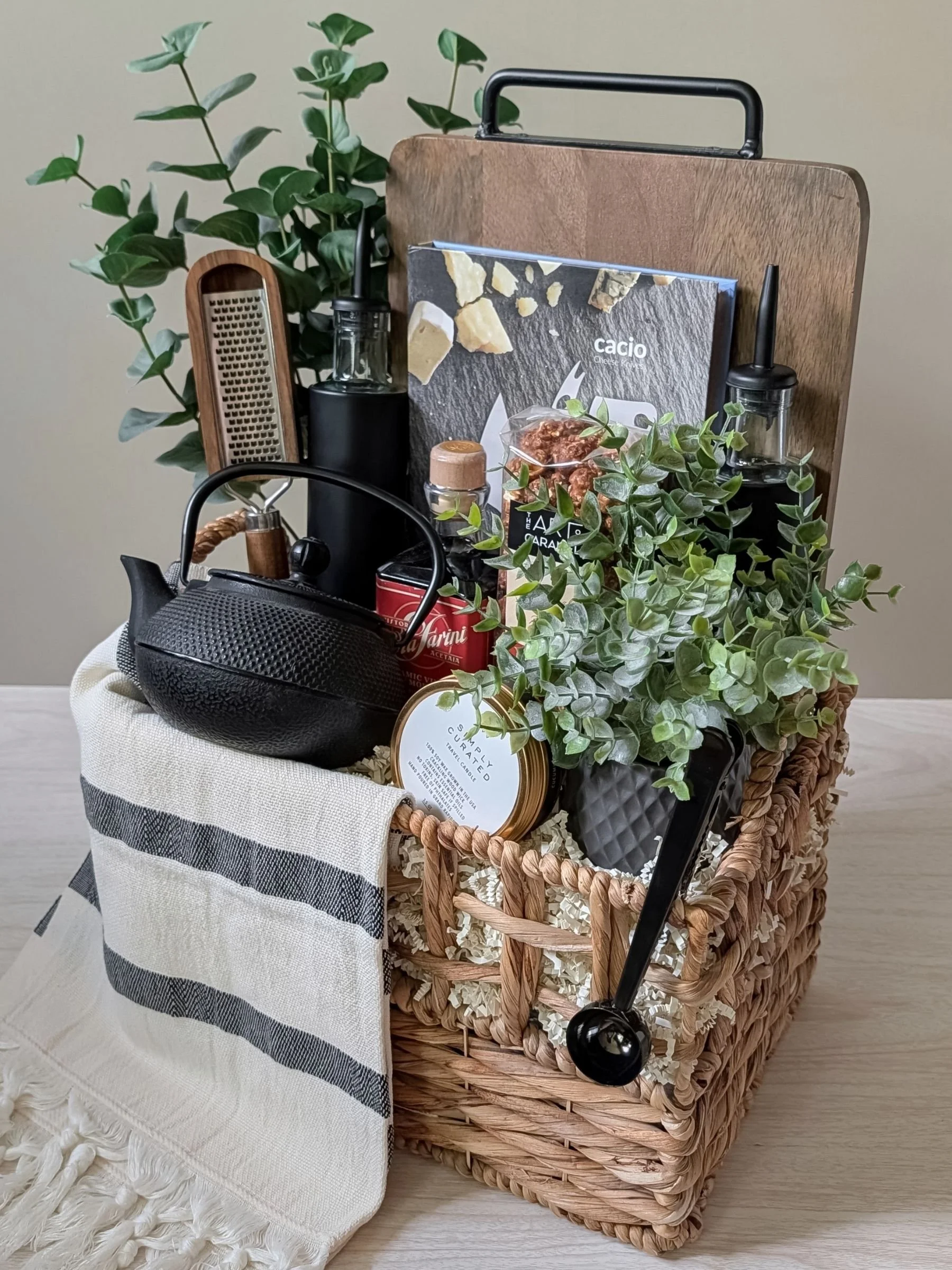Design‑forward gift basket with a cast iron teapot, luxe black oil dispensers, wood grater, luxe candle, and refined kitchen essentials.