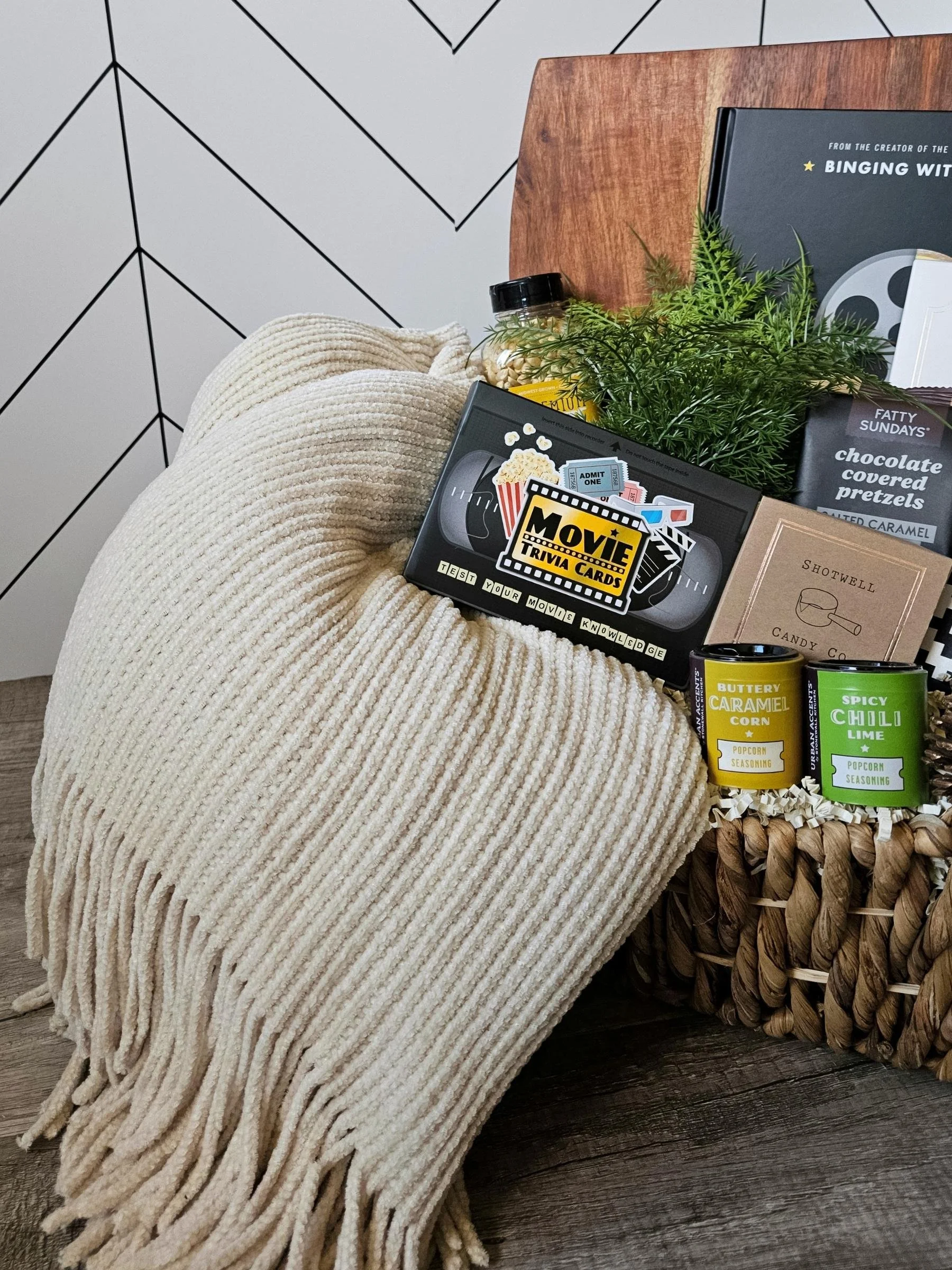 Curated movie‑night gift box featuring a soft throw, gourmet snacks, popcorn seasonings, a film‑inspired cookbook, and movie trivia.