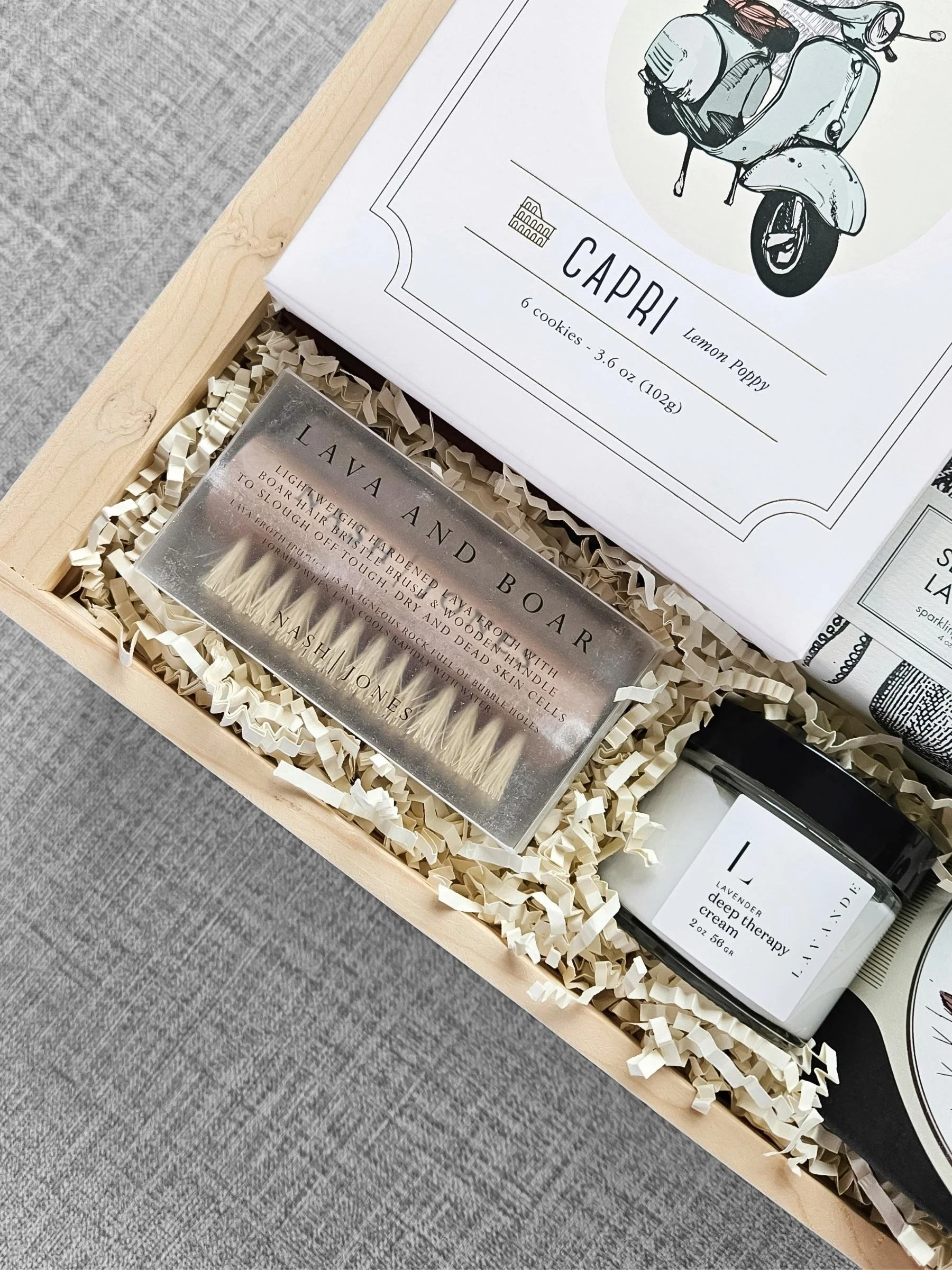 Luxury gift box with lemon poppy shortbread cookies, a wood serving board, a boar and lava brush, and a tea strainer styled together.