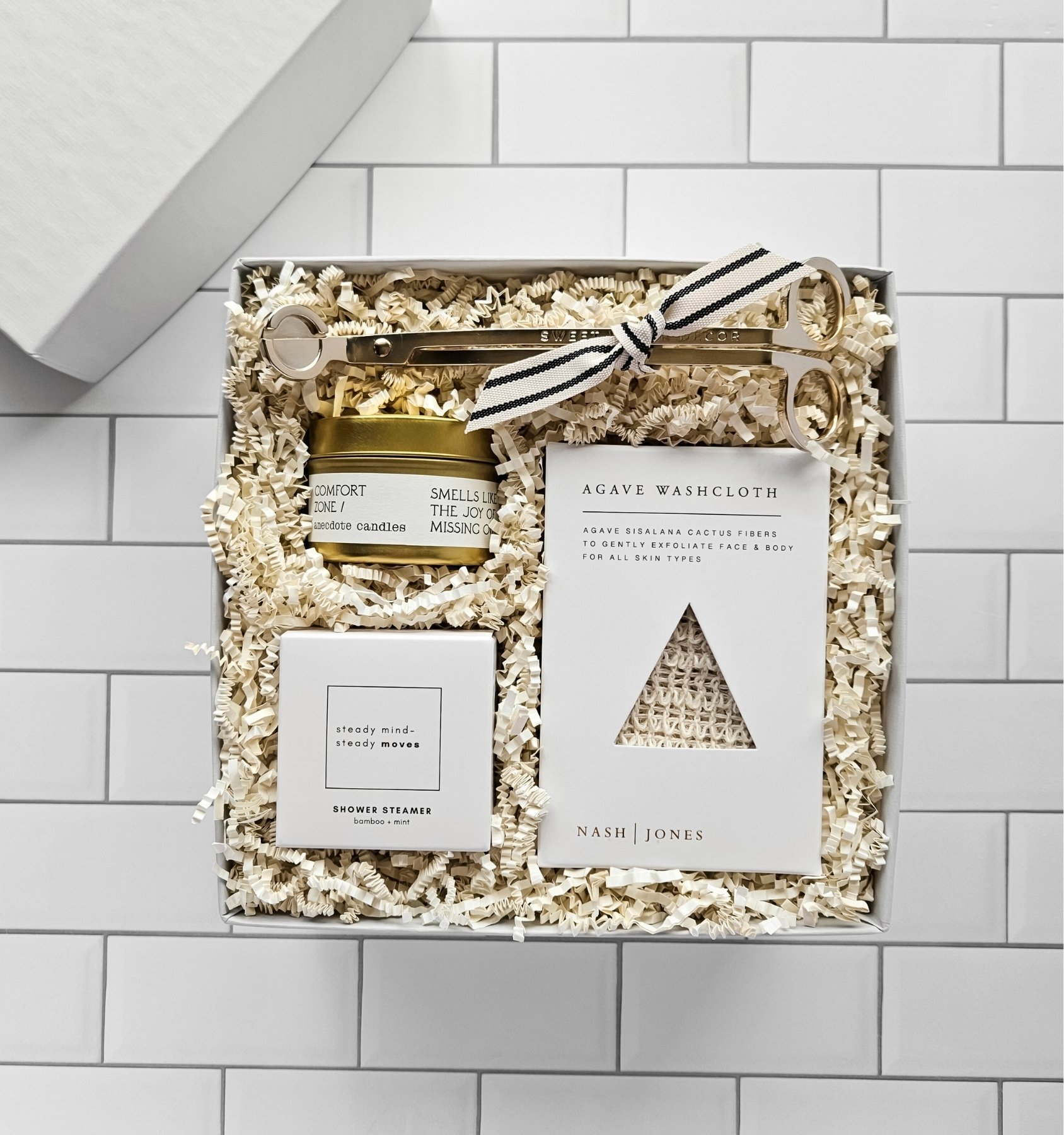 Luxury self‑care gift box featuring candle, shower steamer, agave washcloth, and gold wick trimmer for relaxation.