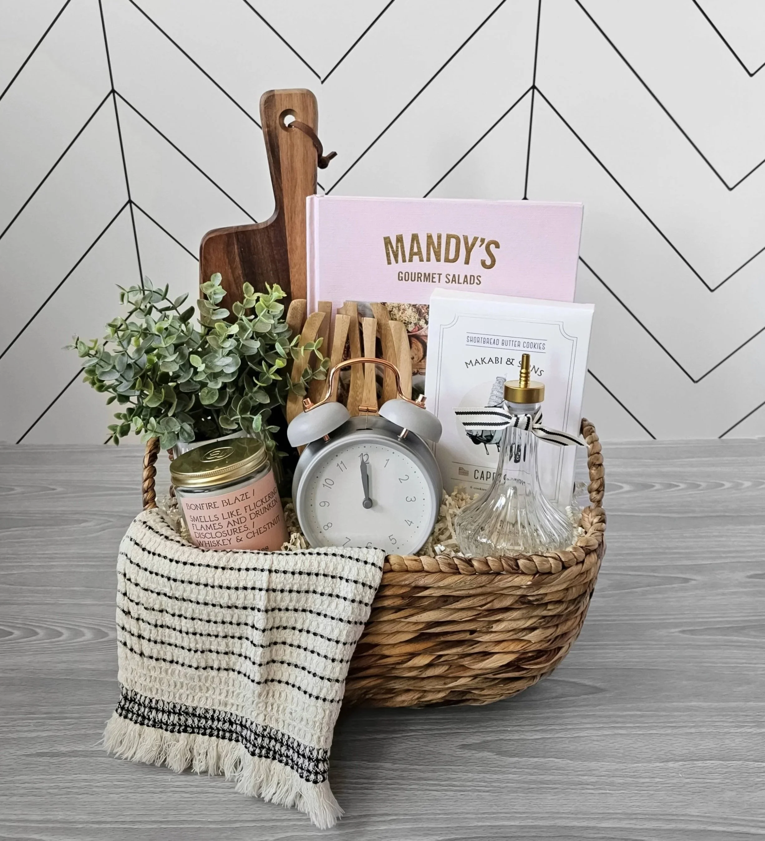 Spring gift basket with pastel kitchen accents, Mandy’s Gourmet Salads book, wood board, candle, cookies, and textured woven hand towel.