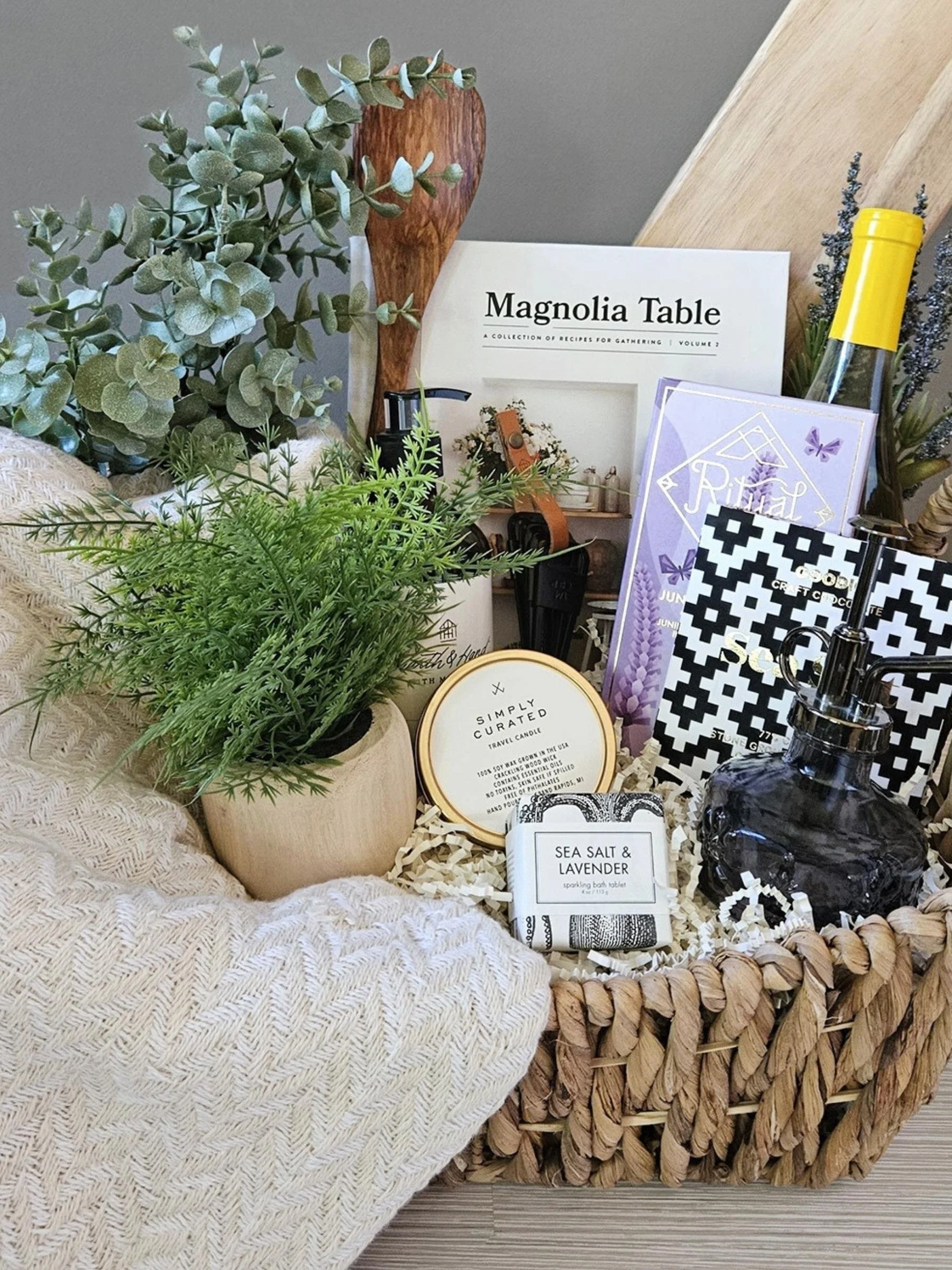 Luxury housewarming gift basket with a Turkish throw, gourmet chocolate, bath bomb, candle, serving board, and elegant home accents.
