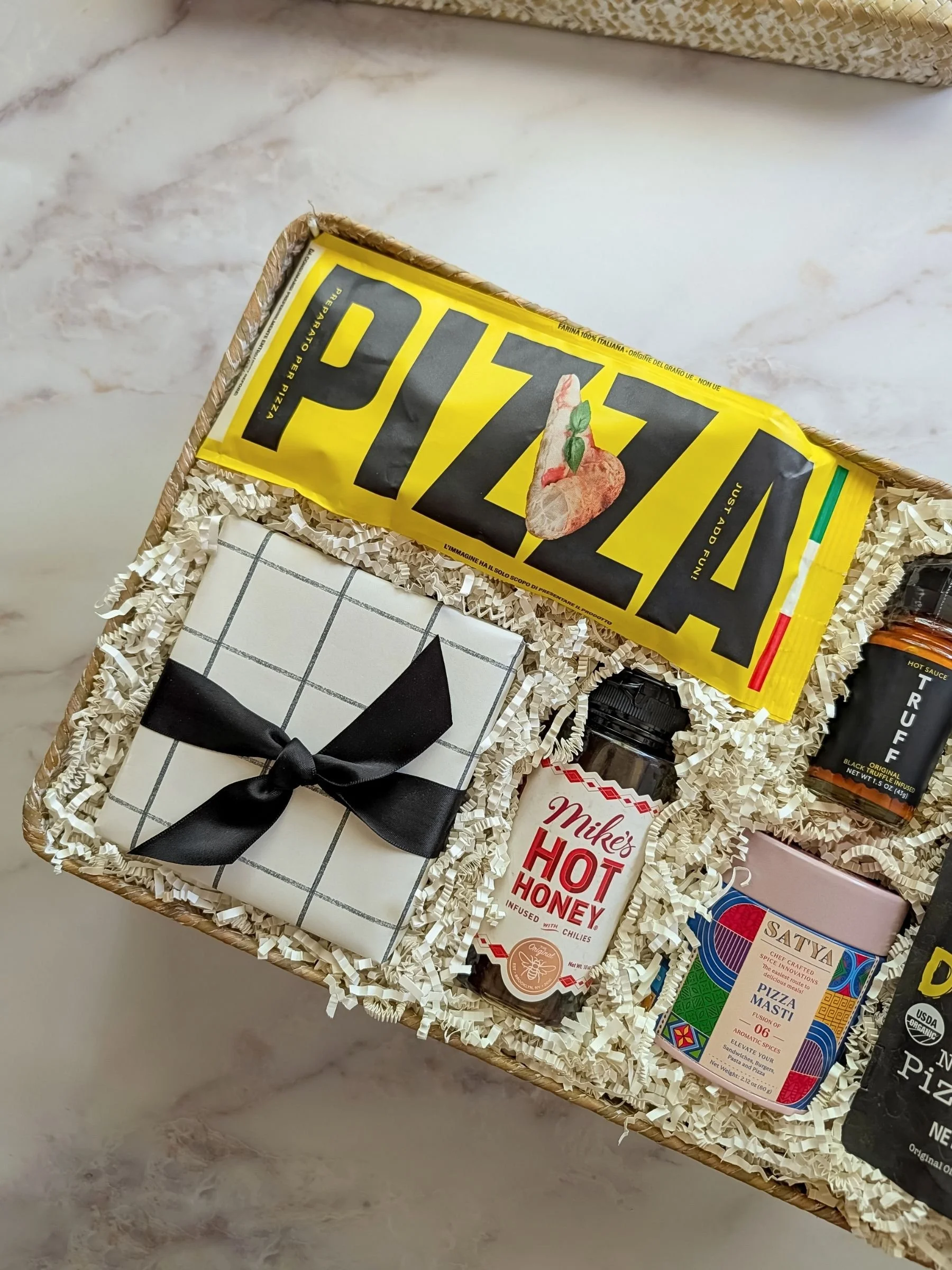 Artisan pizza gift basket filled with authentic Italian pizza dough, gourmet pizza seasoning, hot honey, and a pizza cutter wrapped in striped paper.
