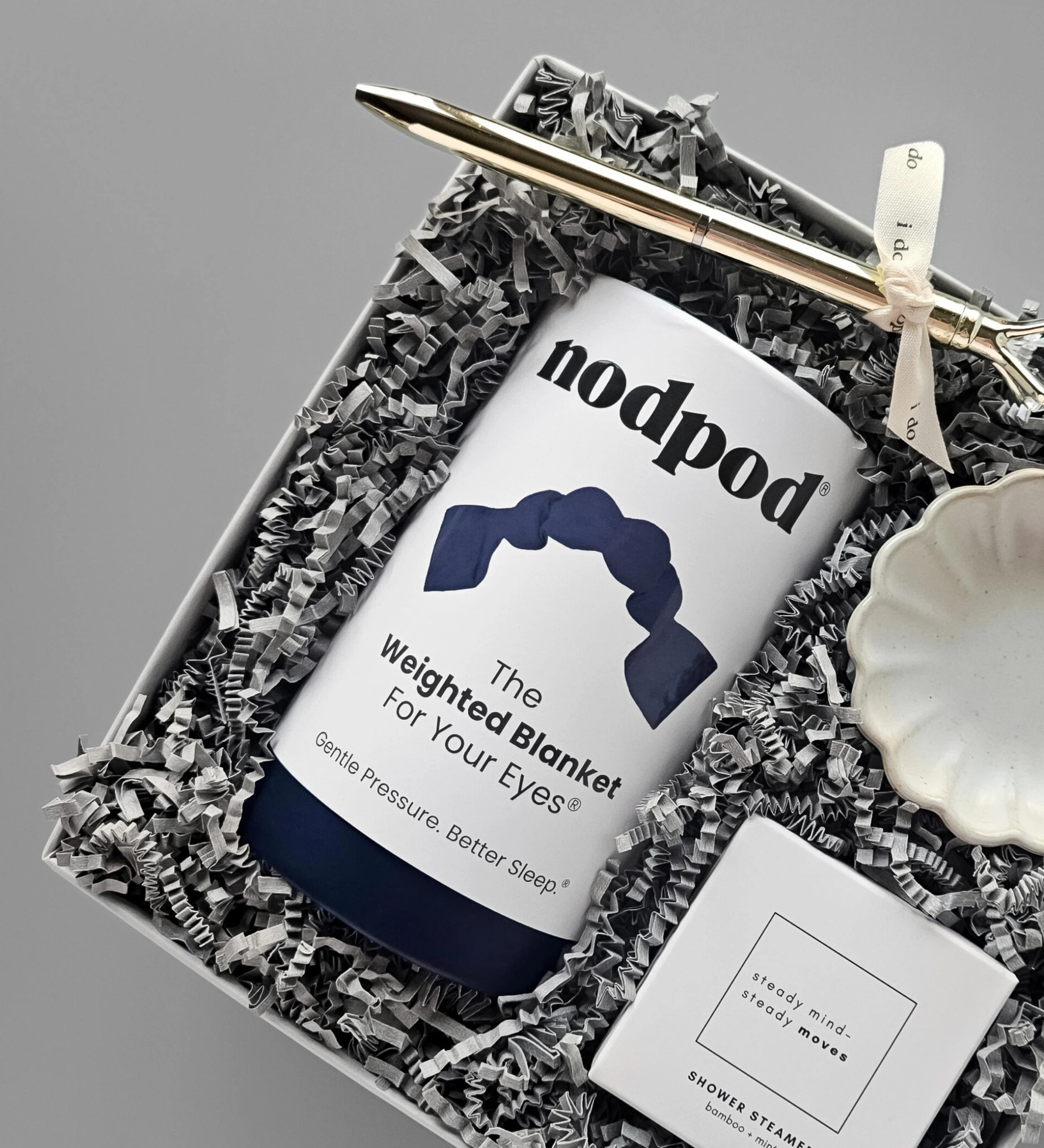 Elegant wedding gift box featuring a midnight blue eye mask, ceramic ring dish, mint shower steamer, and gold “I do” pen.