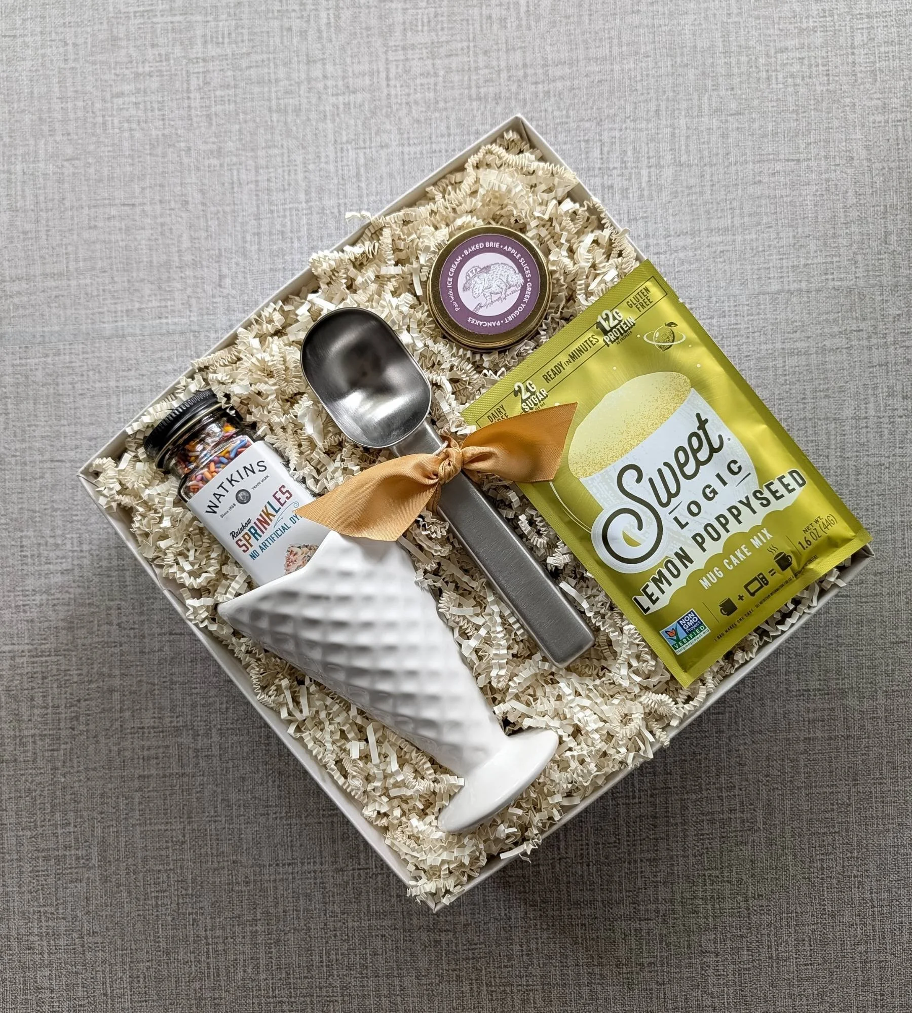 Ice‑cream‑inspired summer gift box with a ceramic white waffle‑cone bowl, premium sprinkles, lemon poppyseed mug cake, caramel sauce, and ice cream scoop.
