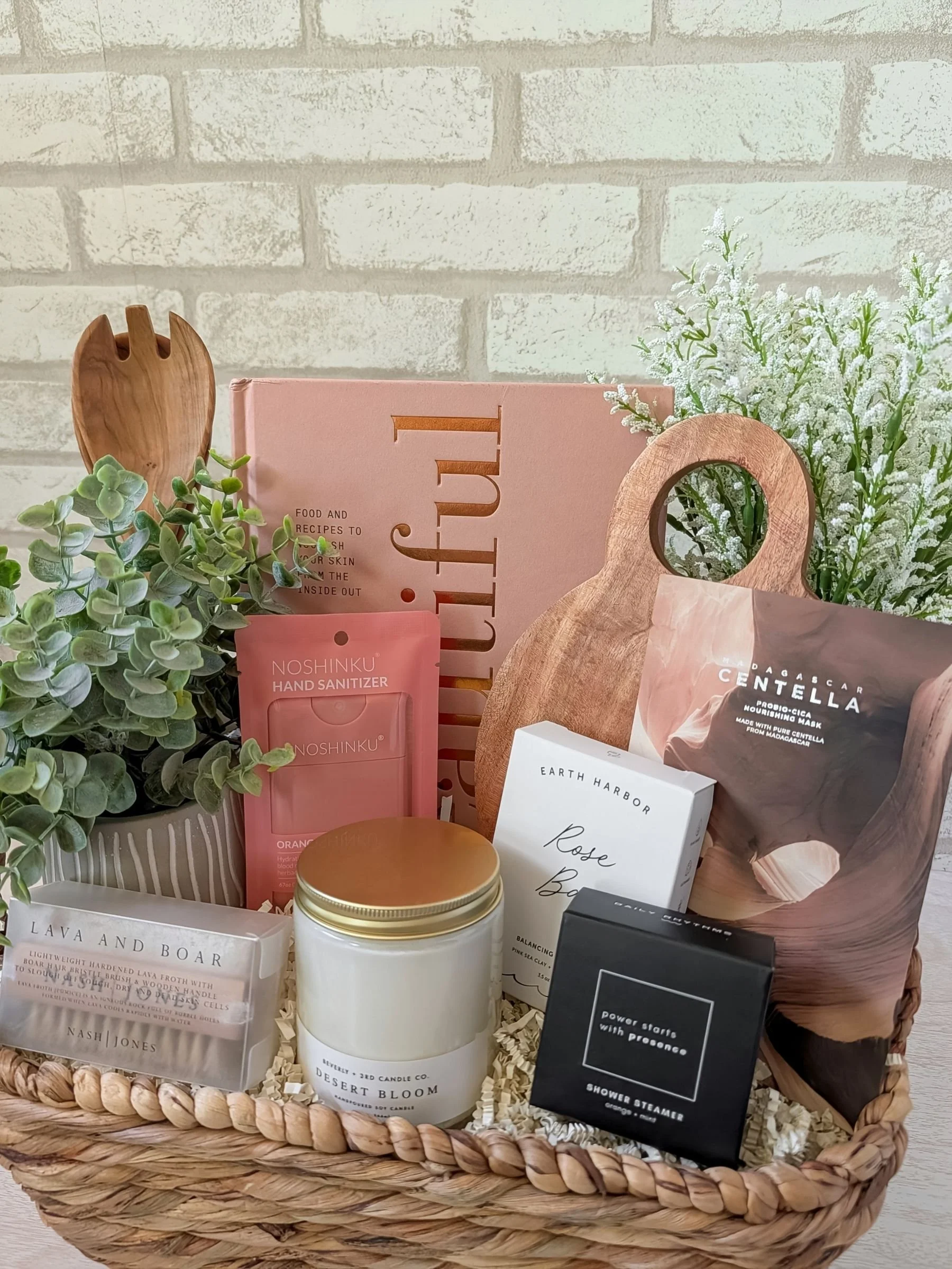 Eat Beautiful gift basket with cookbook, skincare, candle, wooden salad spoons, and wellness items in a woven seagrass basket.
