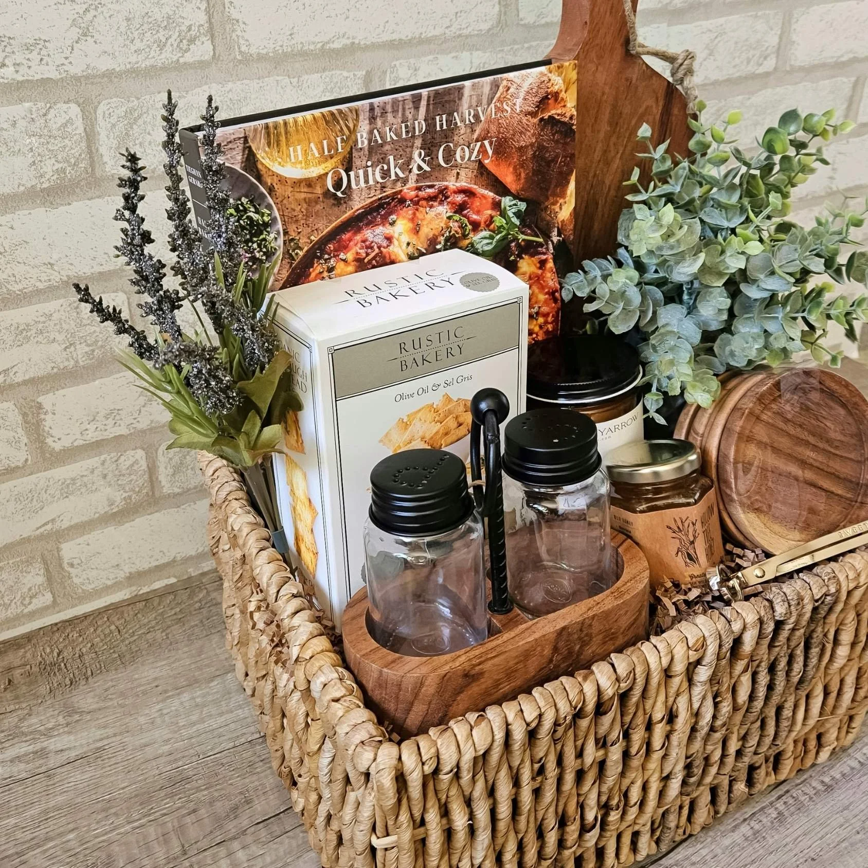 Cozy fall inspired gift basket with cookbook, salt & pepper shakers, wood serving board, and gourmet treats.