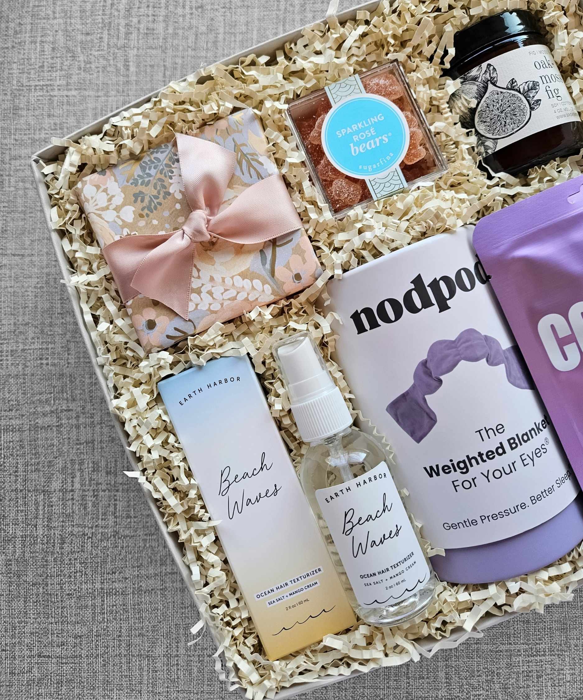 Luxury self‑care gift box with weighted eye mask, beach wave spray, candle, champagne gummies, collagen mask, and eye gels.
