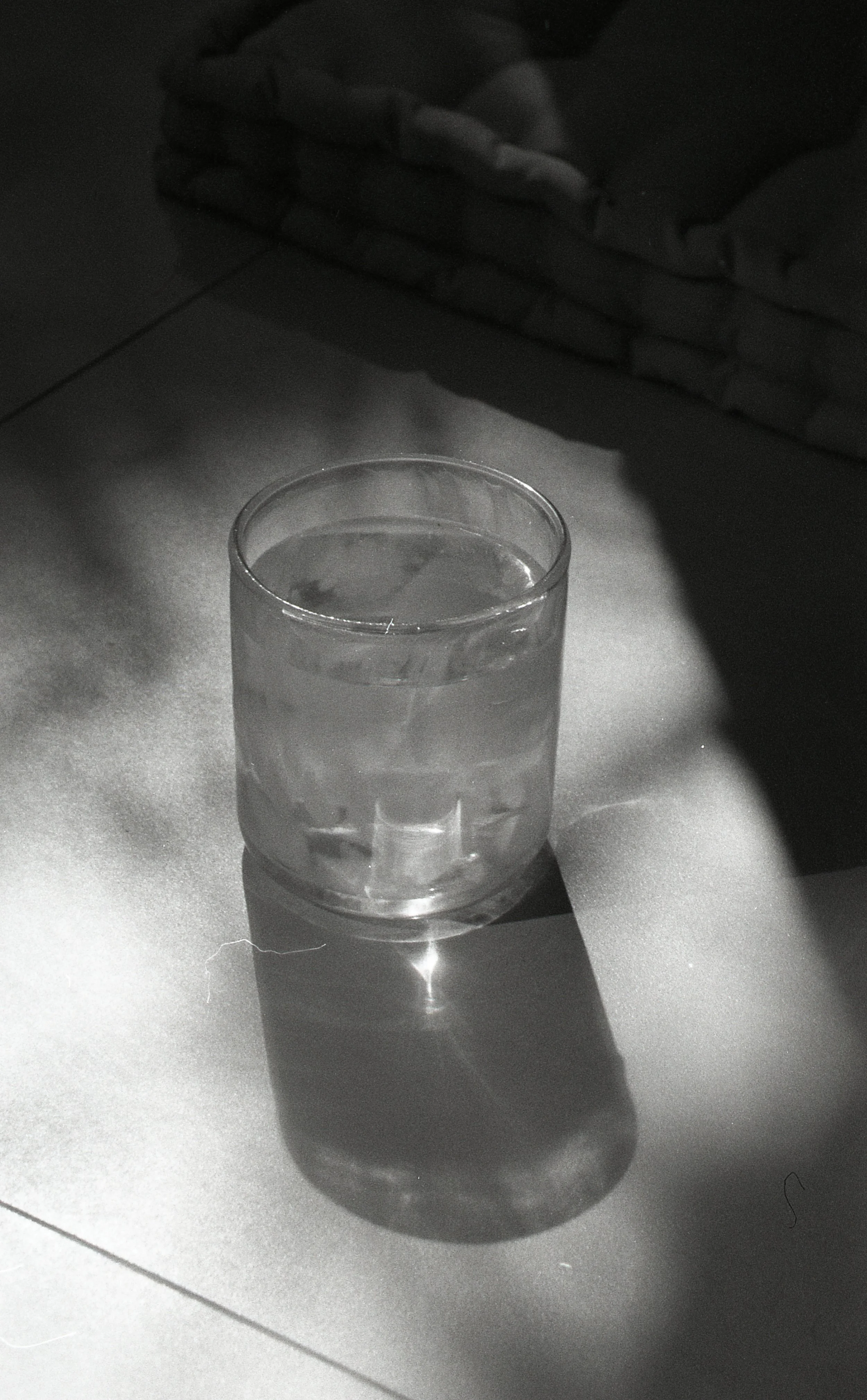 A glass of water used during healing sessions, on a surface with shadow, in black and white.