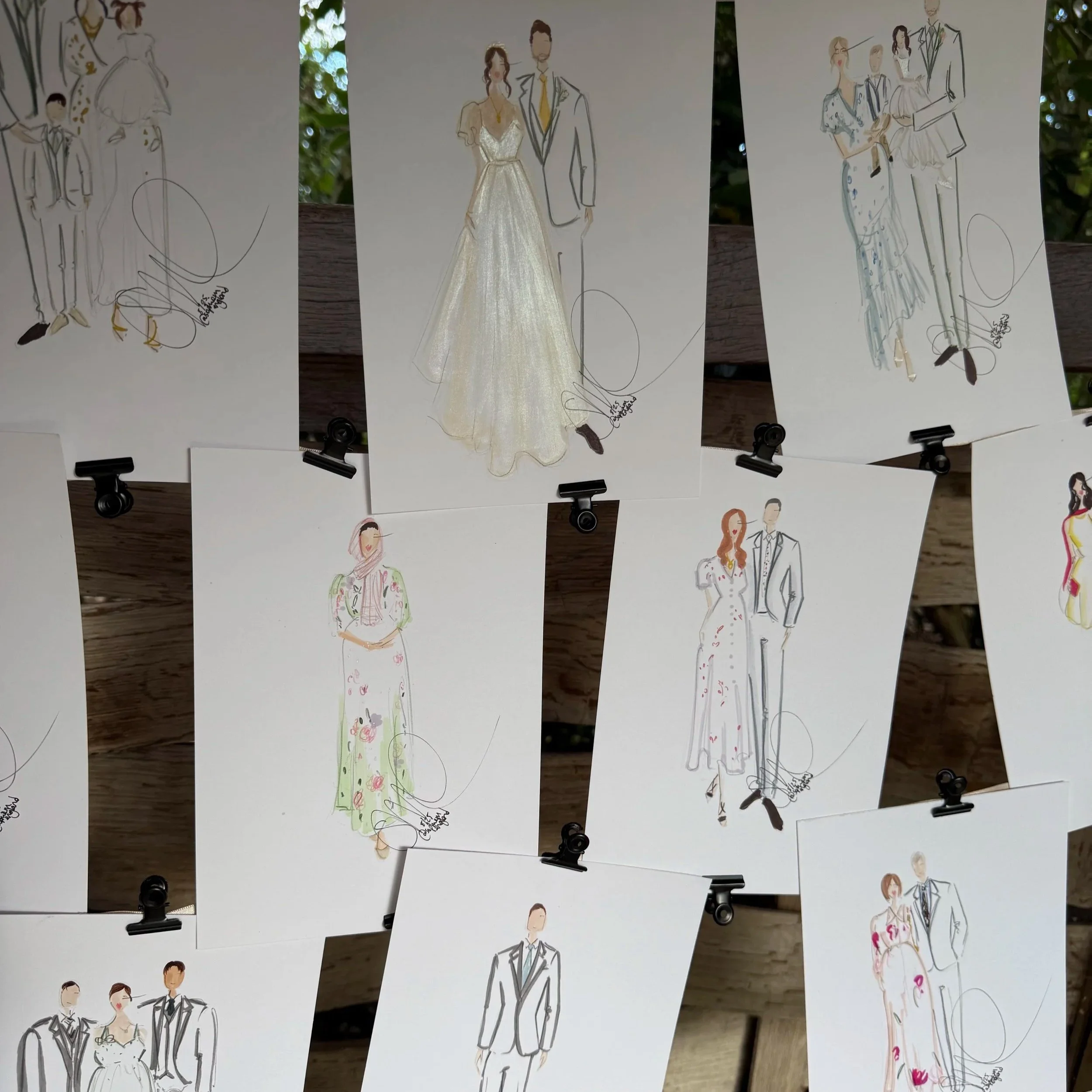 Collection of fashion illustrations featuring women in wedding dresses and men in suits, hanging on a clothesline with black clips outdoors.