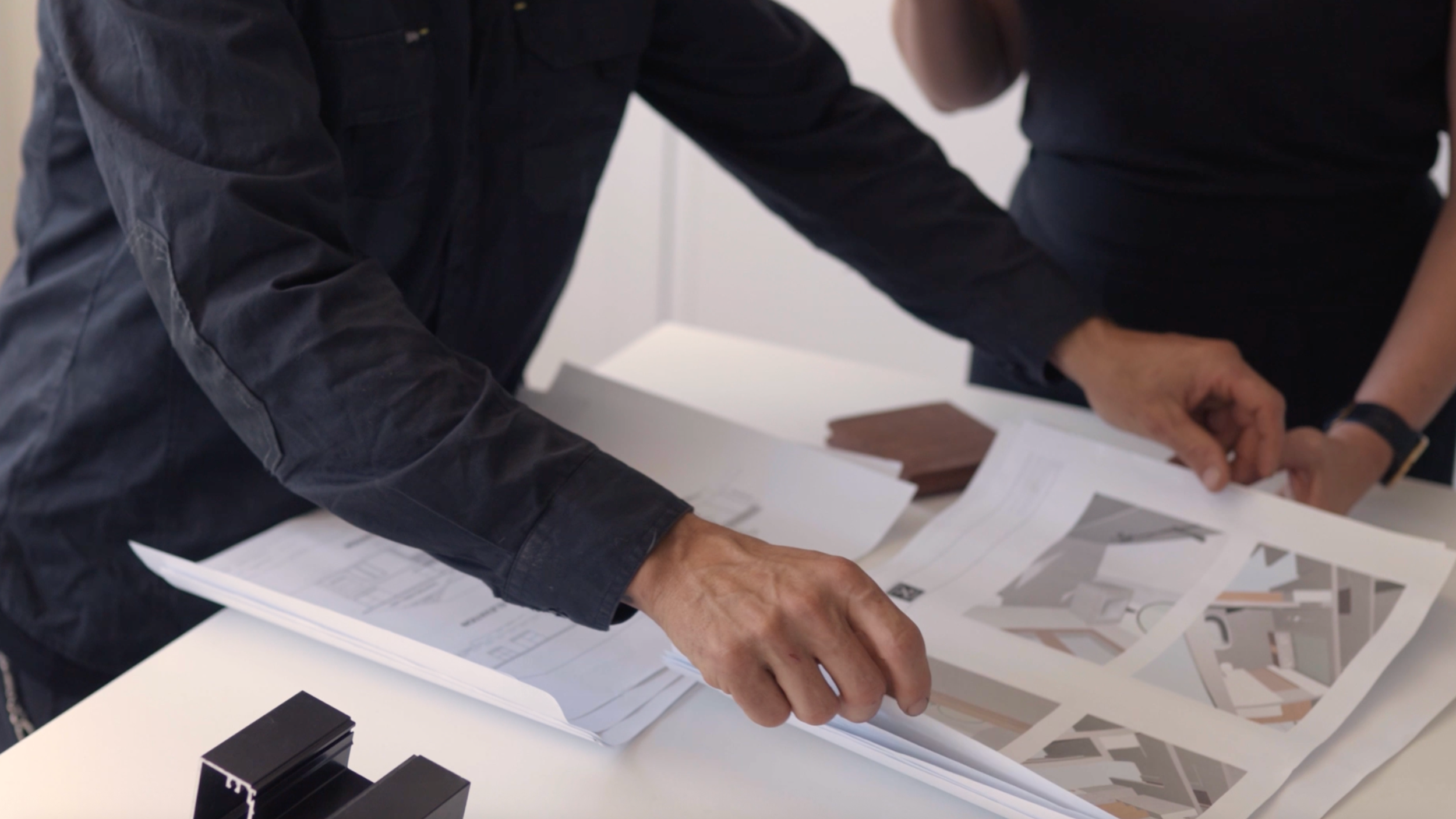 Two people reviewing architectural plans and documents on a white table, with design samples and printed images, in an office setting.