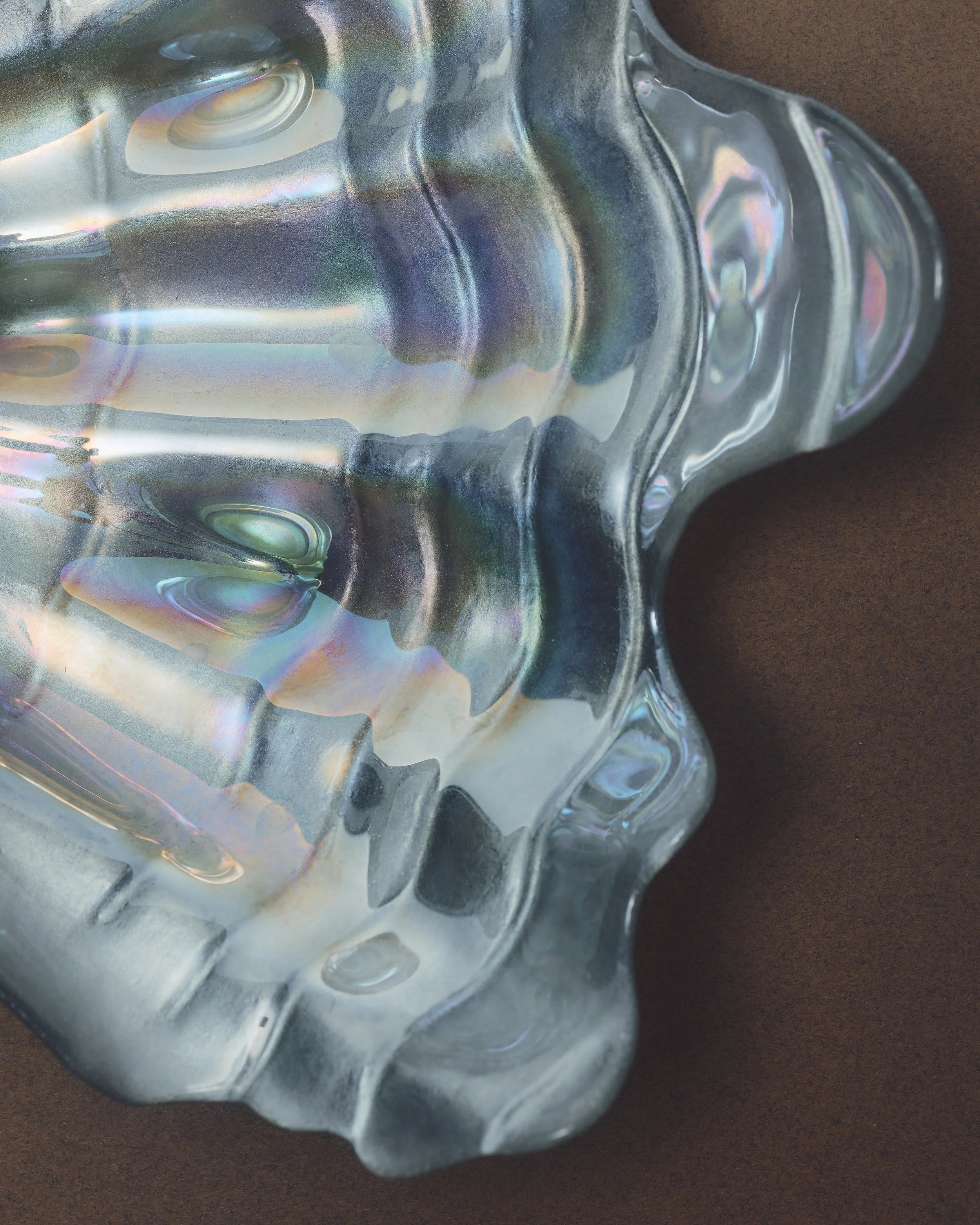 Close-up of iridescent glass bowl with wavy edges on a brown surface.