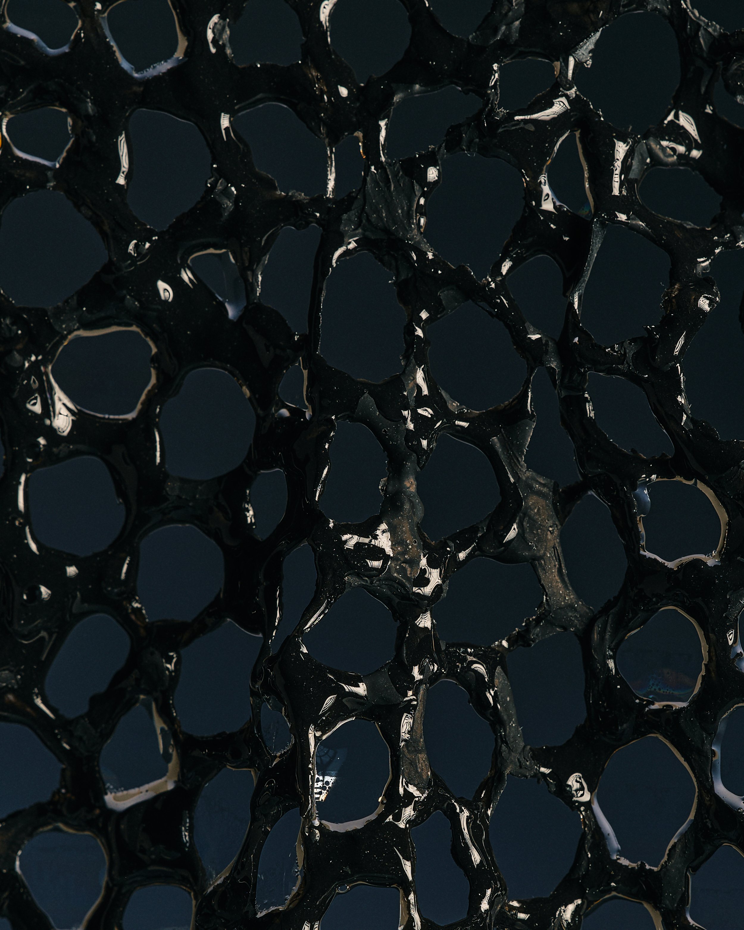 Close-up of a black honeycomb-like structure with shiny, reflective surfaces set against a dark background.