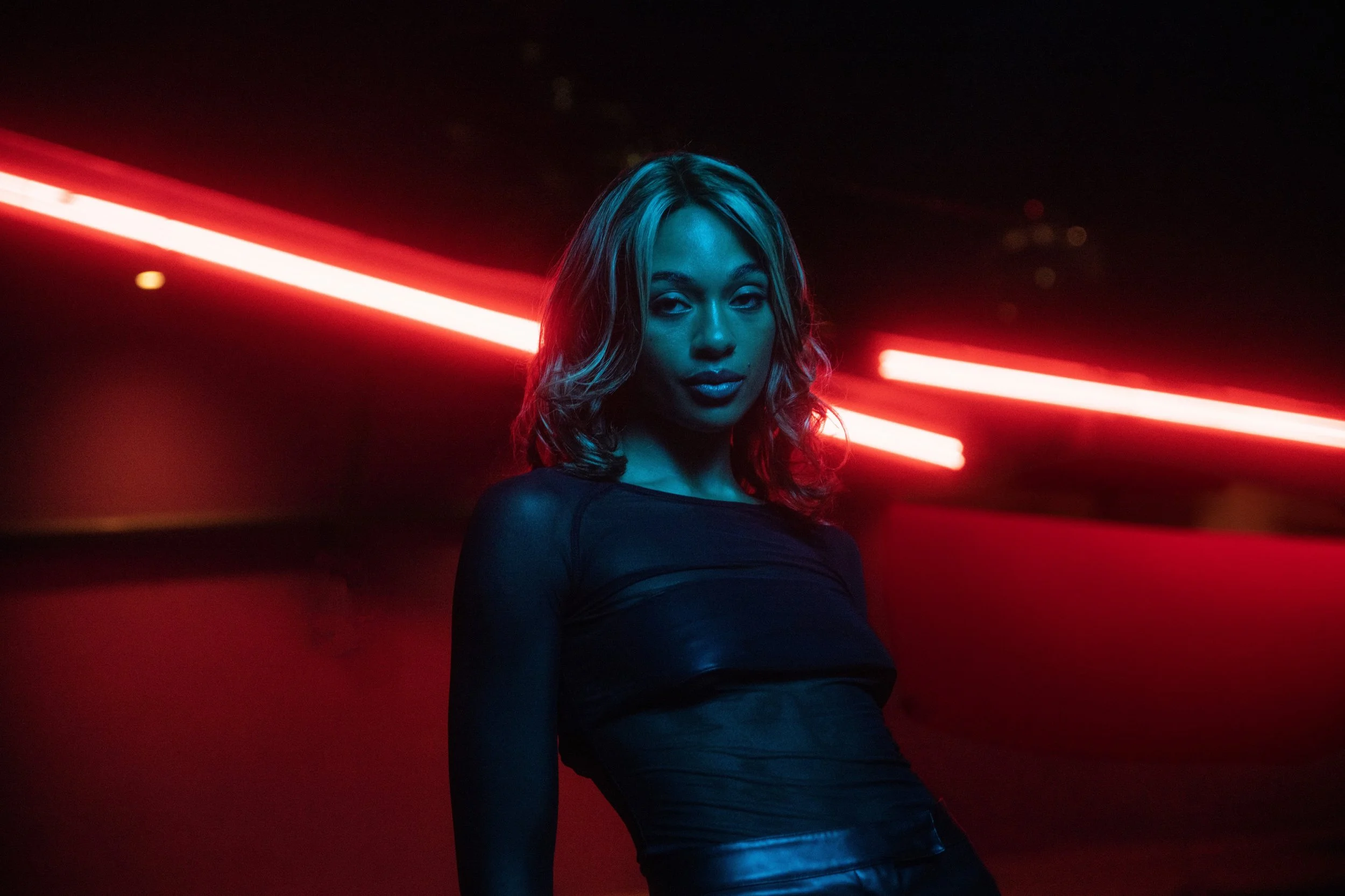 A woman with shoulder-length hair standing in front of two red light beams in a dark environment
