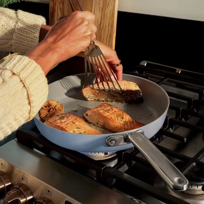 Salmon cooking in a blue Ninja NeverQuit ceramic-coated skillet on a gas stovetop.
