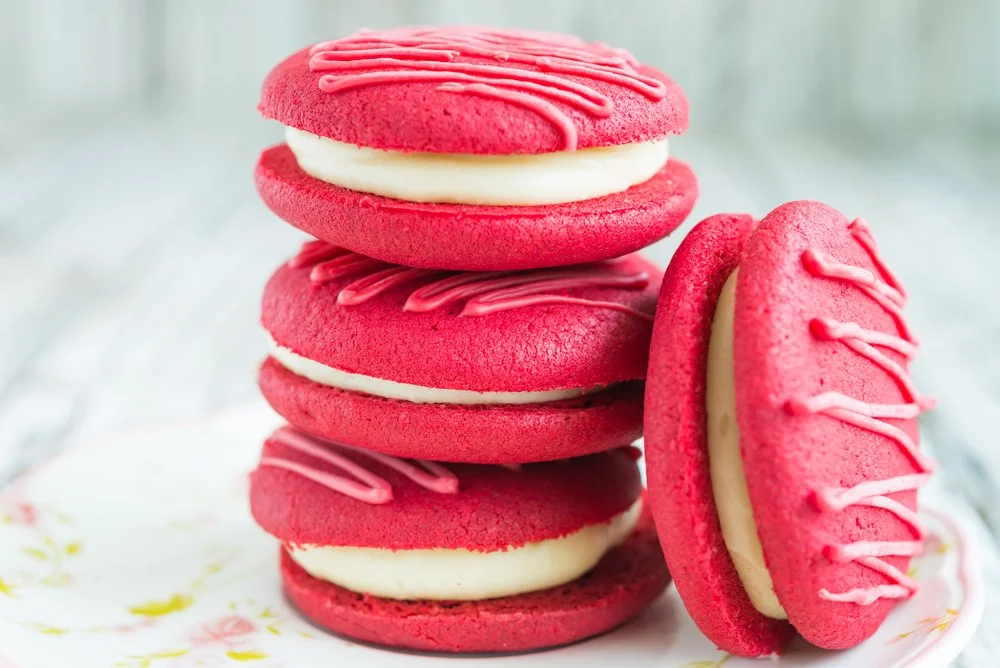 Red velvet whoopie pies filled with white cream and drizzled with red icing.