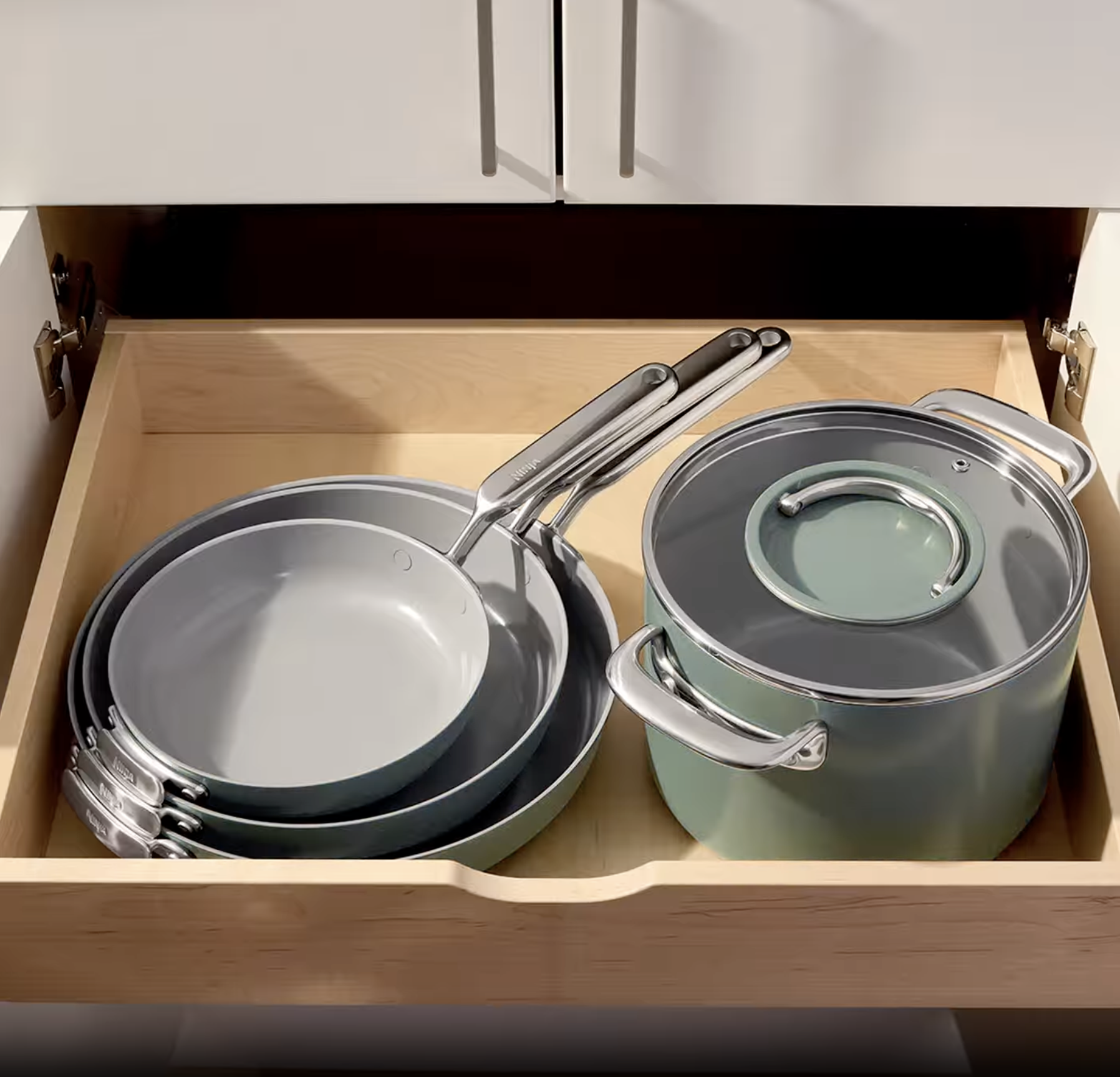 Forest Sage Ninja NeverQuit cookware nested with LayFlat lids in a kitchen drawer.