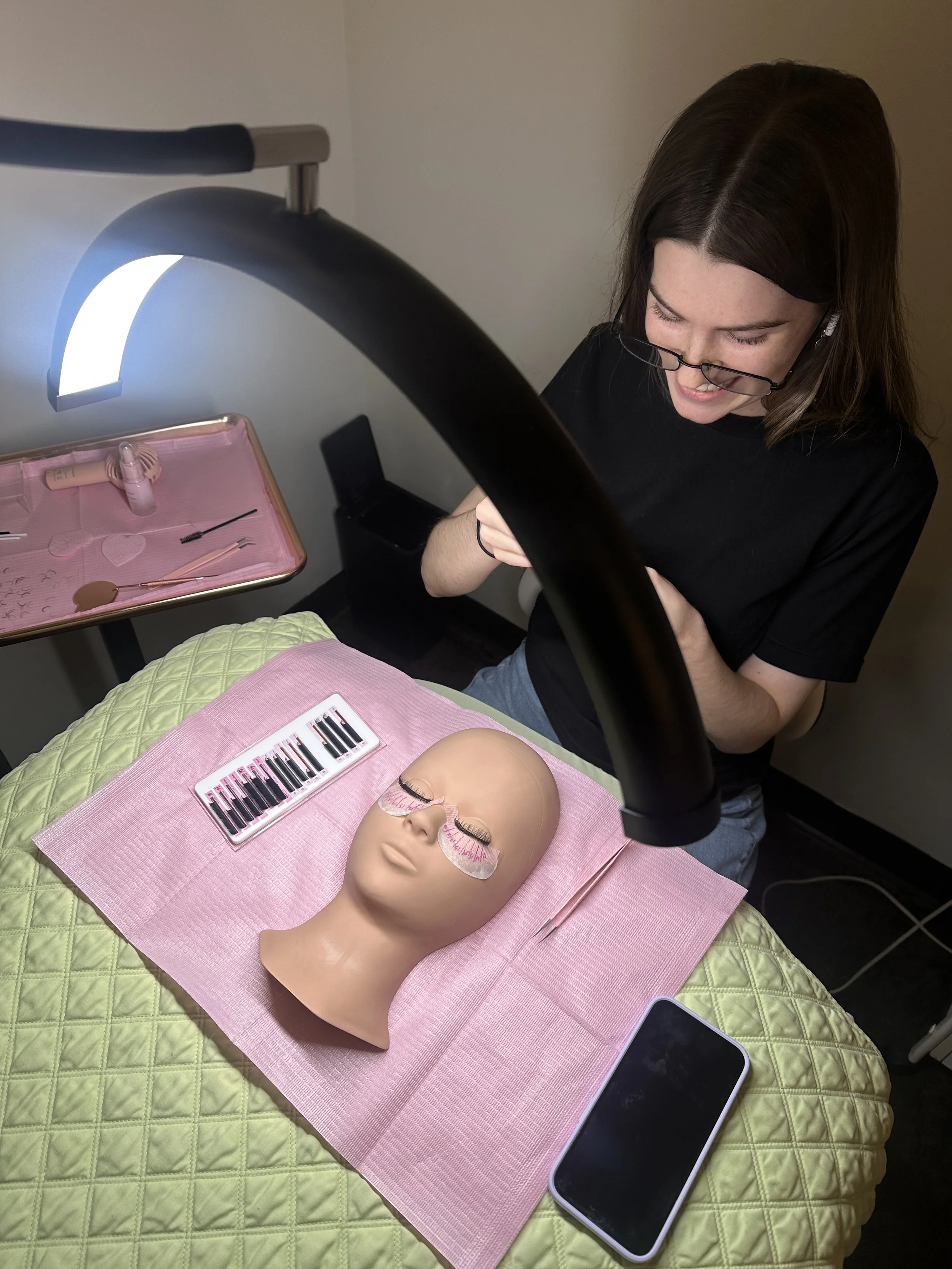 Student sitting down with a lash lamp over her working on her mannequin